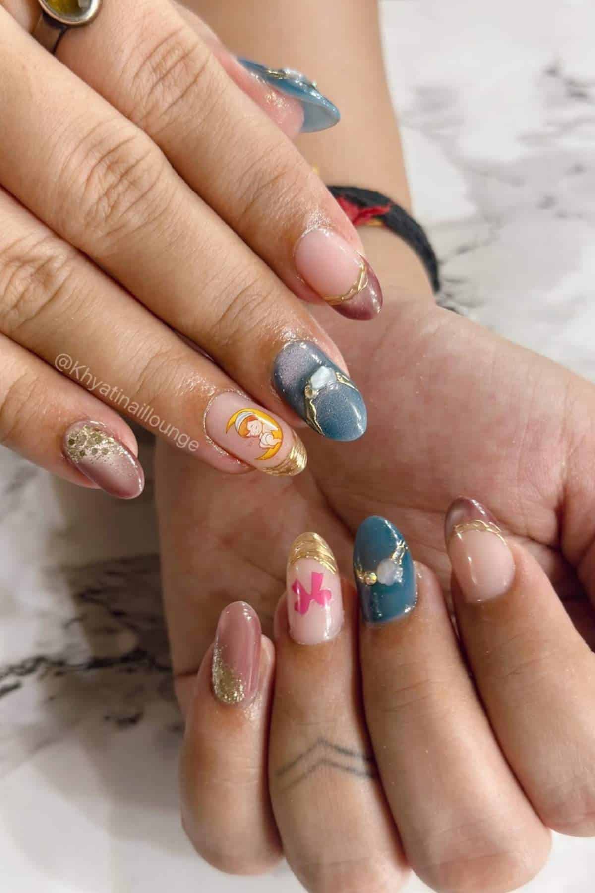 Hands with almond-shaped nails featuring various designs, including gold accents, blue polish, a cartoon character, a pink bow, and decorative nail art on a marble surface.