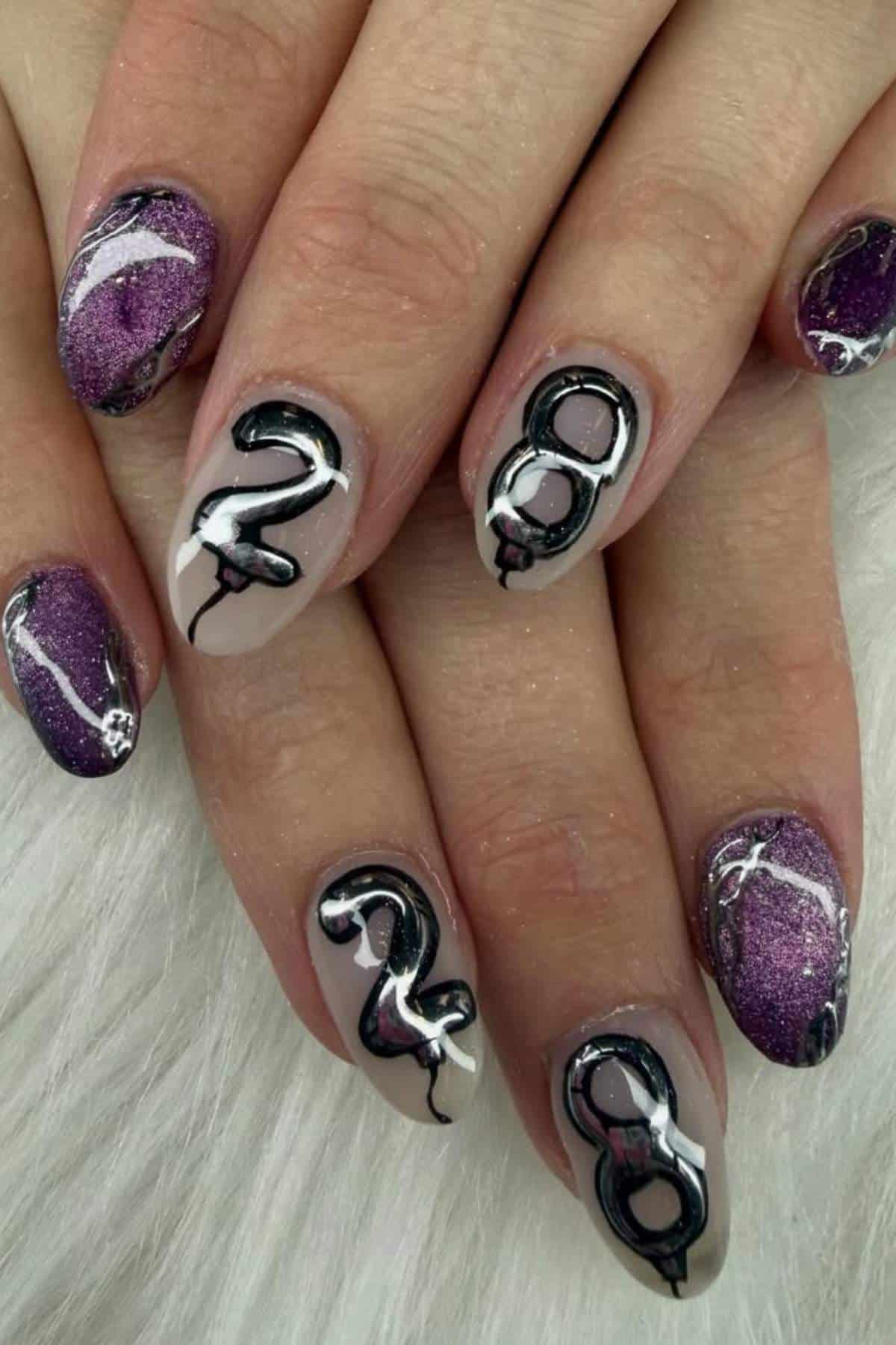 A hand with manicured nails; some are painted purple with metallic accents while others are nude with black and white 3D numbers "2" and "8" on them.