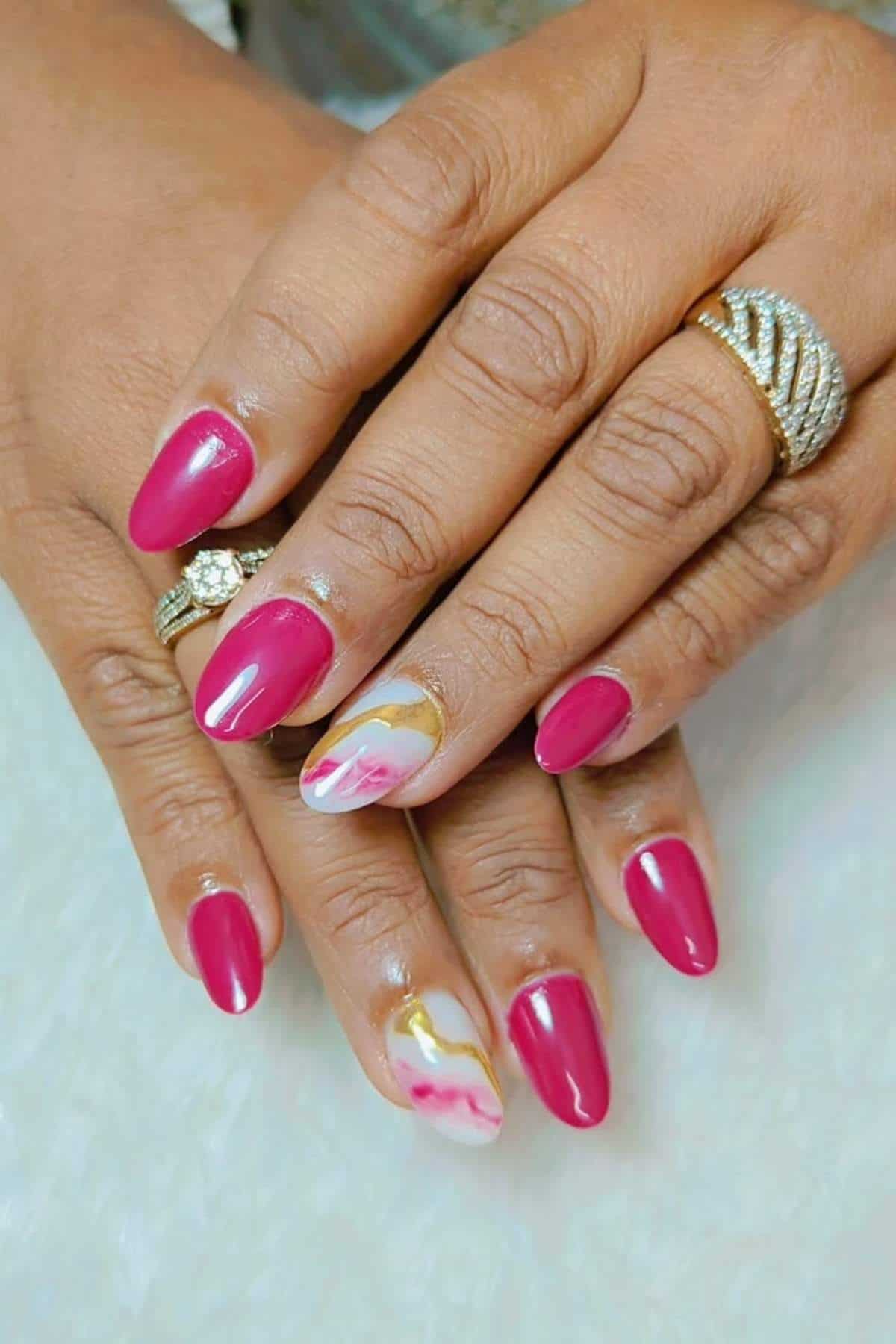 Close-up of hands with pink manicured nails, gold rings, and two accent nails featuring a marble design in white, pink, and gold.