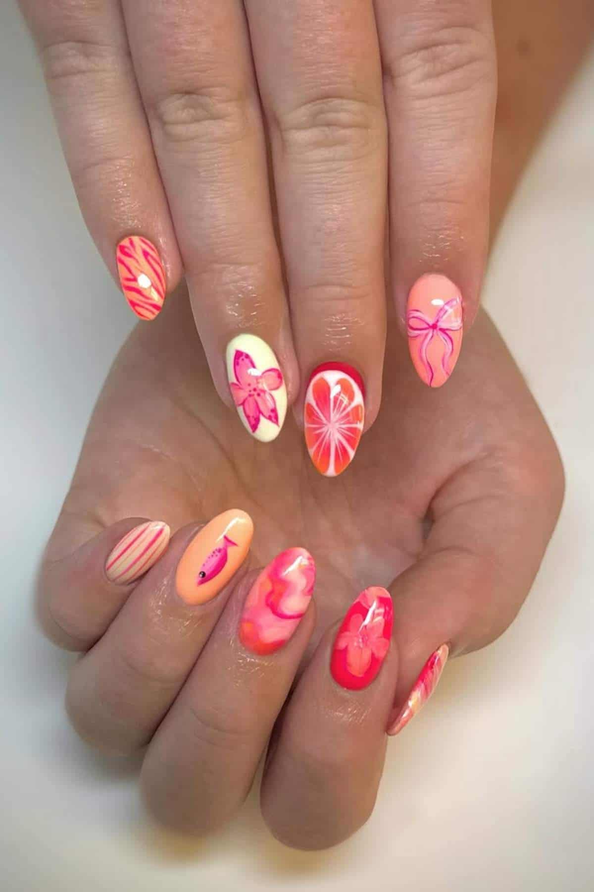 Hands with long almond-shaped nails painted in pink, orange, and white shades featuring designs of butterflies, hearts, swirls, and abstract patterns.