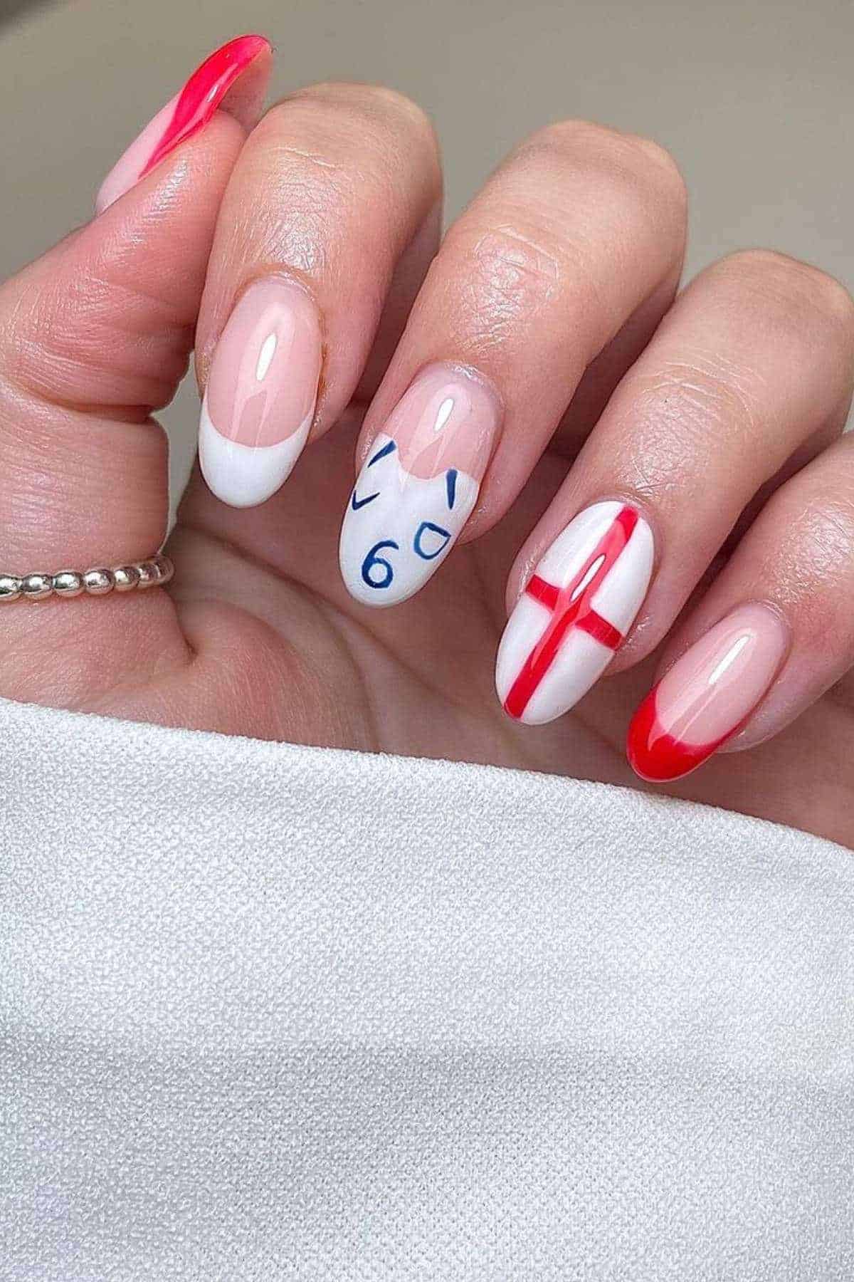 A hand with manicured nails featuring white and red French tips, an England flag design, and a blue number 6 with a football shirt outline on the middle finger.