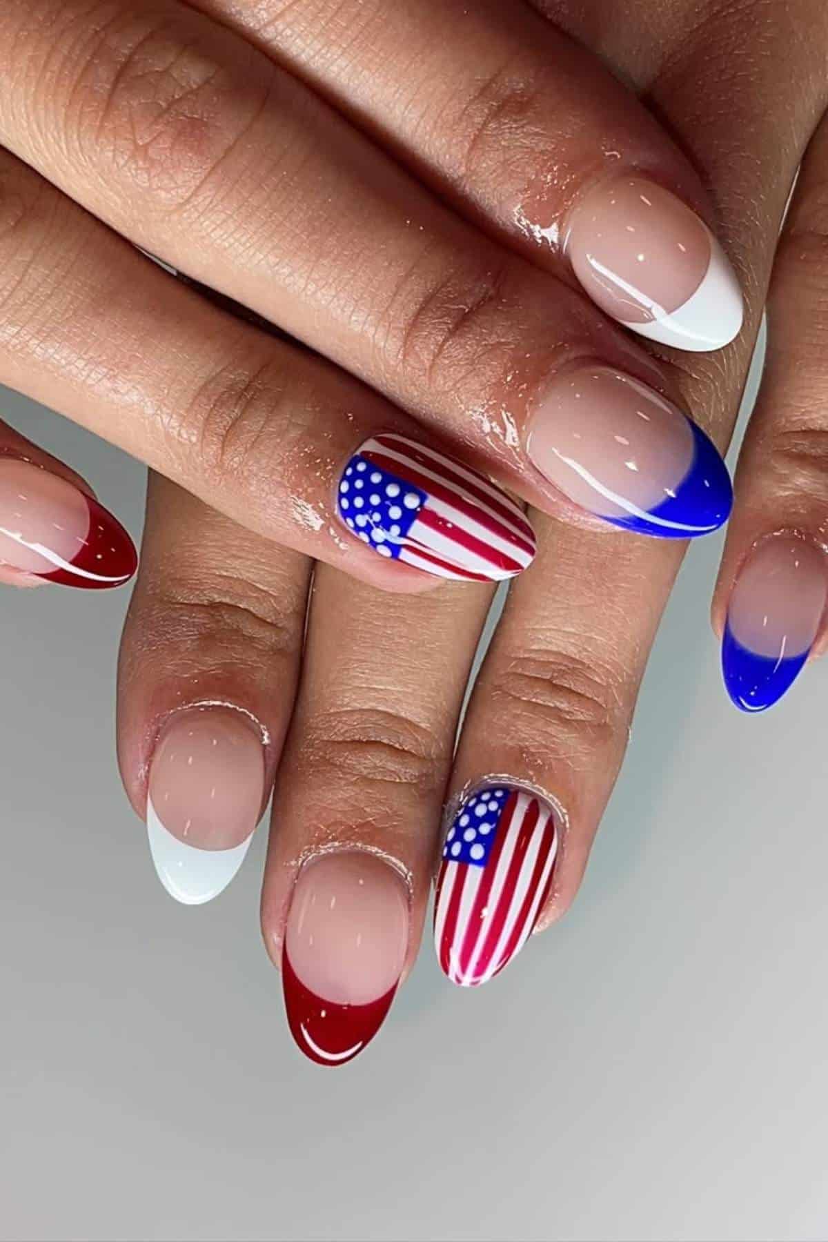 A hand with manicured nails featuring a French tip design in red, white, and blue, with two accent nails painted as the American flag.