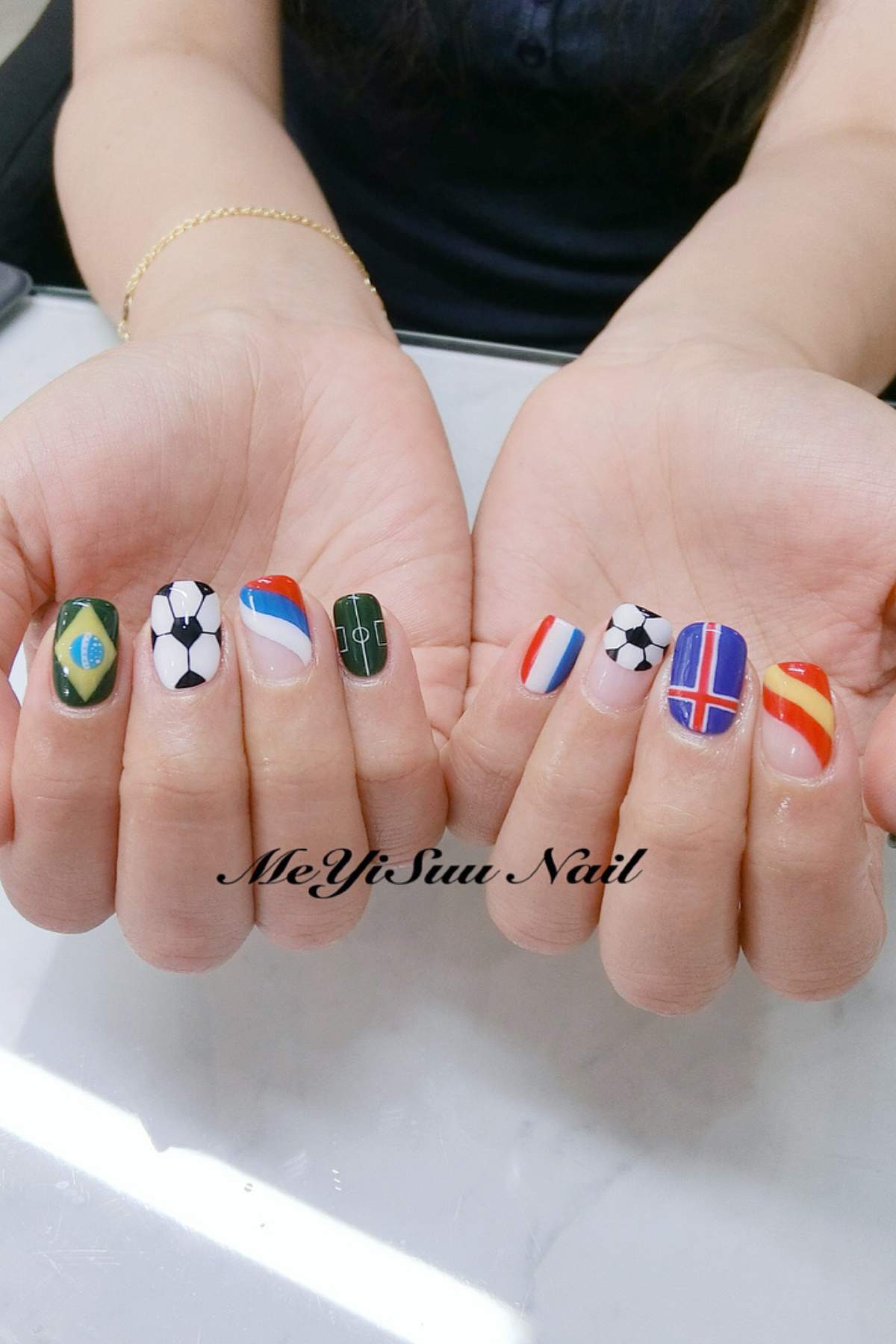 A pair of hands with manicured nails painted with soccer and international flag designs, including soccer balls, a field, and various country flags.