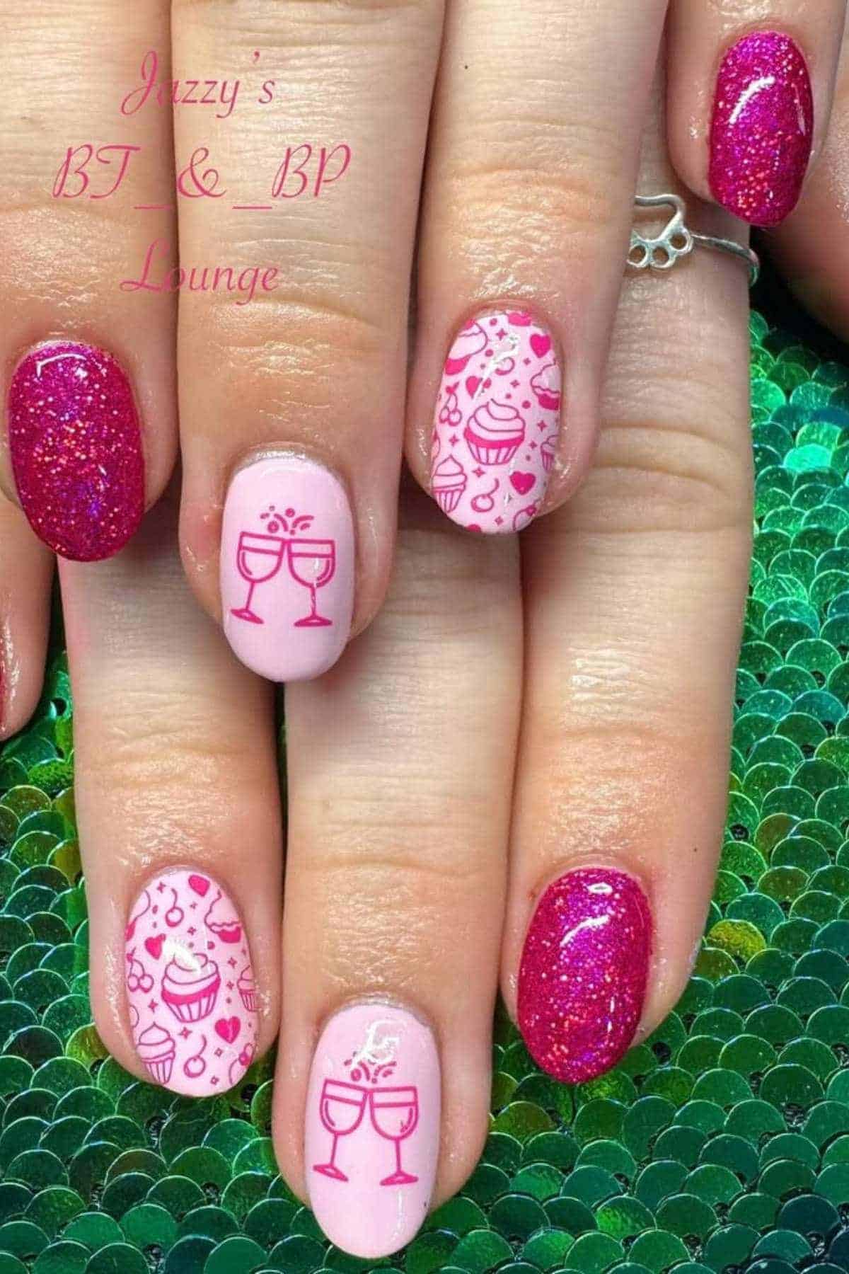 Fingernails with pink glitter polish and light pink polish featuring wine glass and celebration-themed designs.