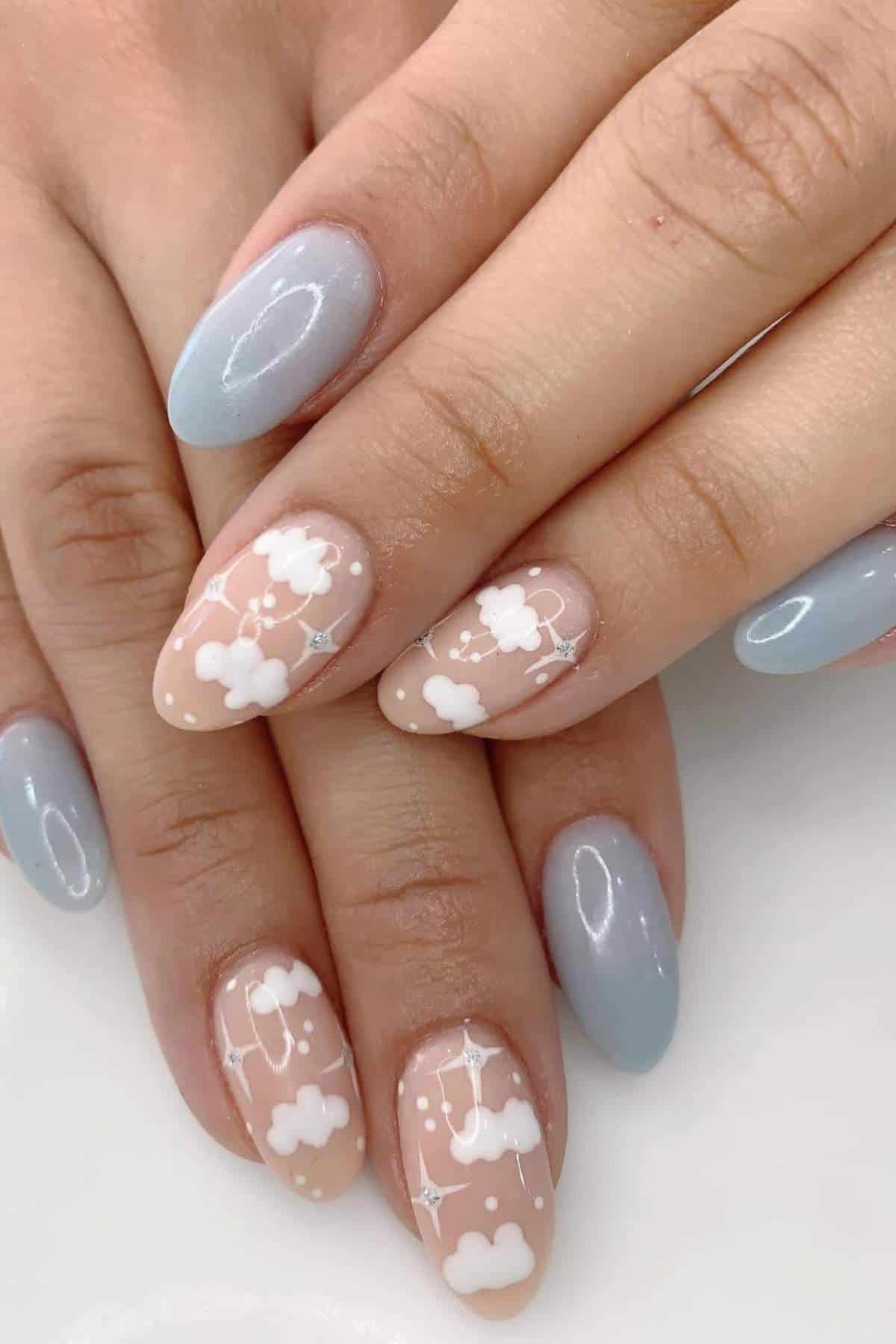 Close-up of hands with manicured nails; some nails are painted light blue, others are nude with white clouds and tiny star designs.