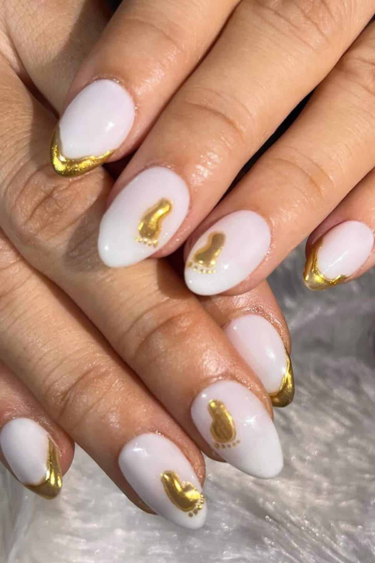 Hands with almond-shaped nails painted white, featuring gold metallic tips and small gold abstract designs on some nails.
