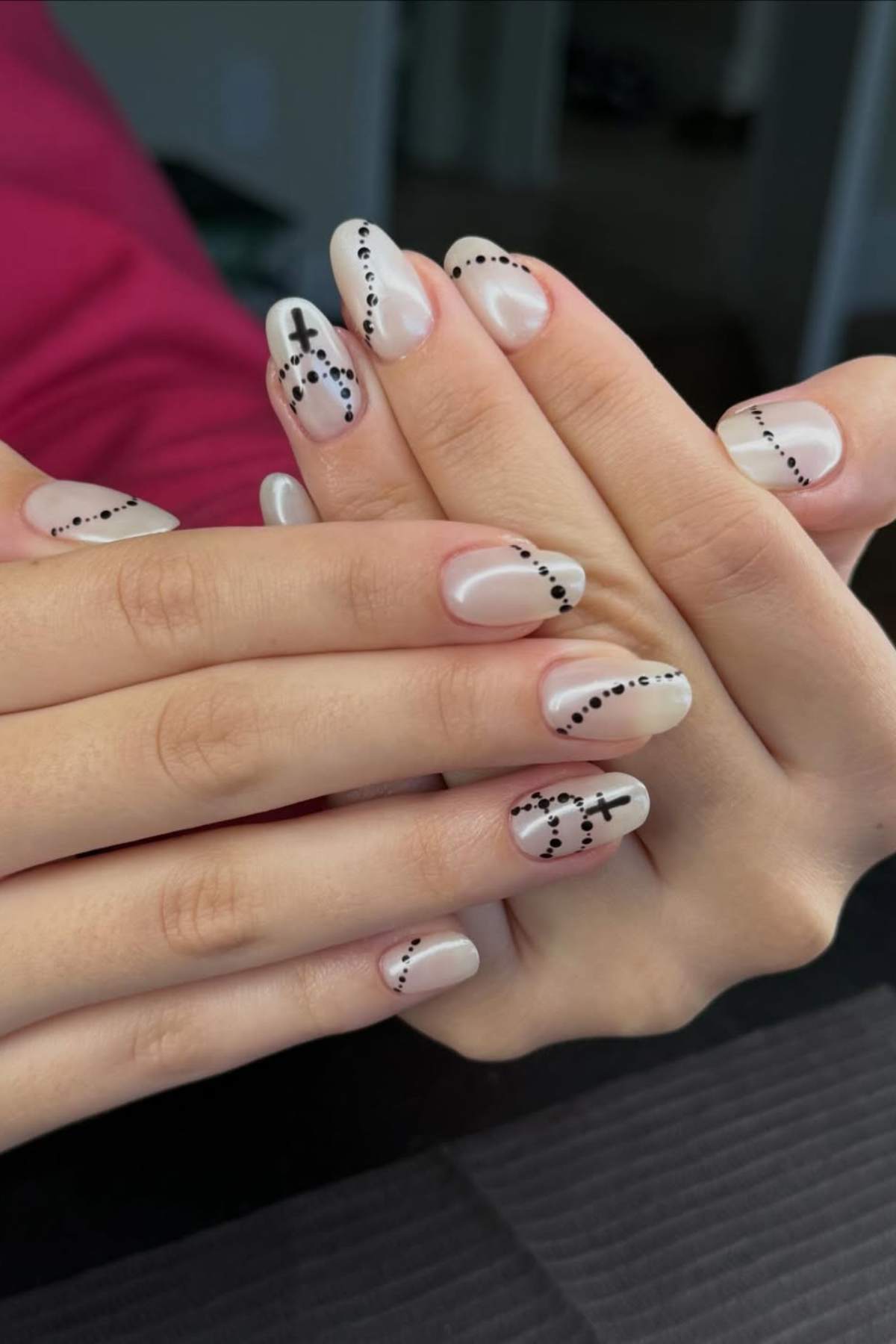 Close-up of hands with nude-colored nails, decorated with black dotted lines forming abstract patterns on each fingernail.