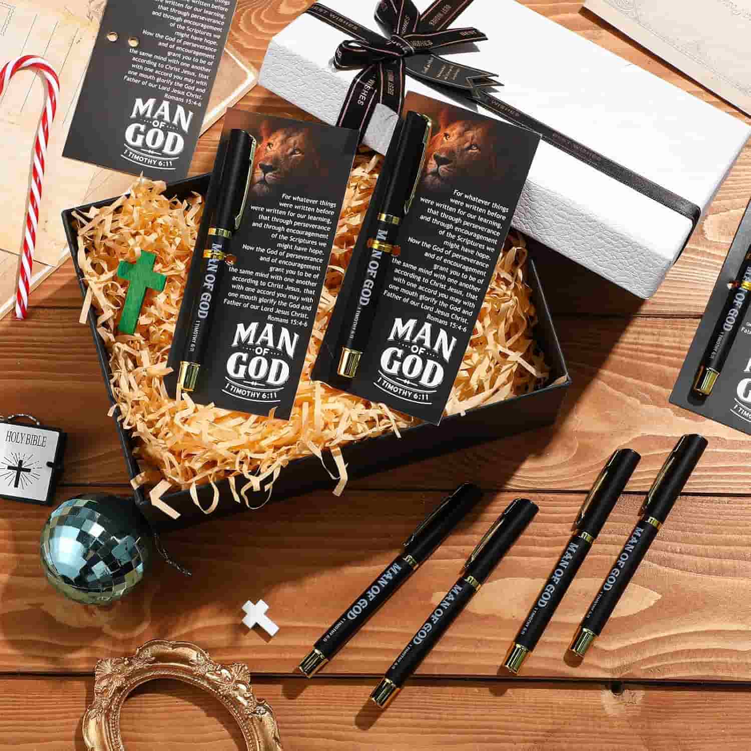 Gift box containing a pen labeled "MAN OF GOD," a bookmark with a lion image, a green cross, decorative straw, and a white wrapped box, with pens and bookmarks scattered nearby.