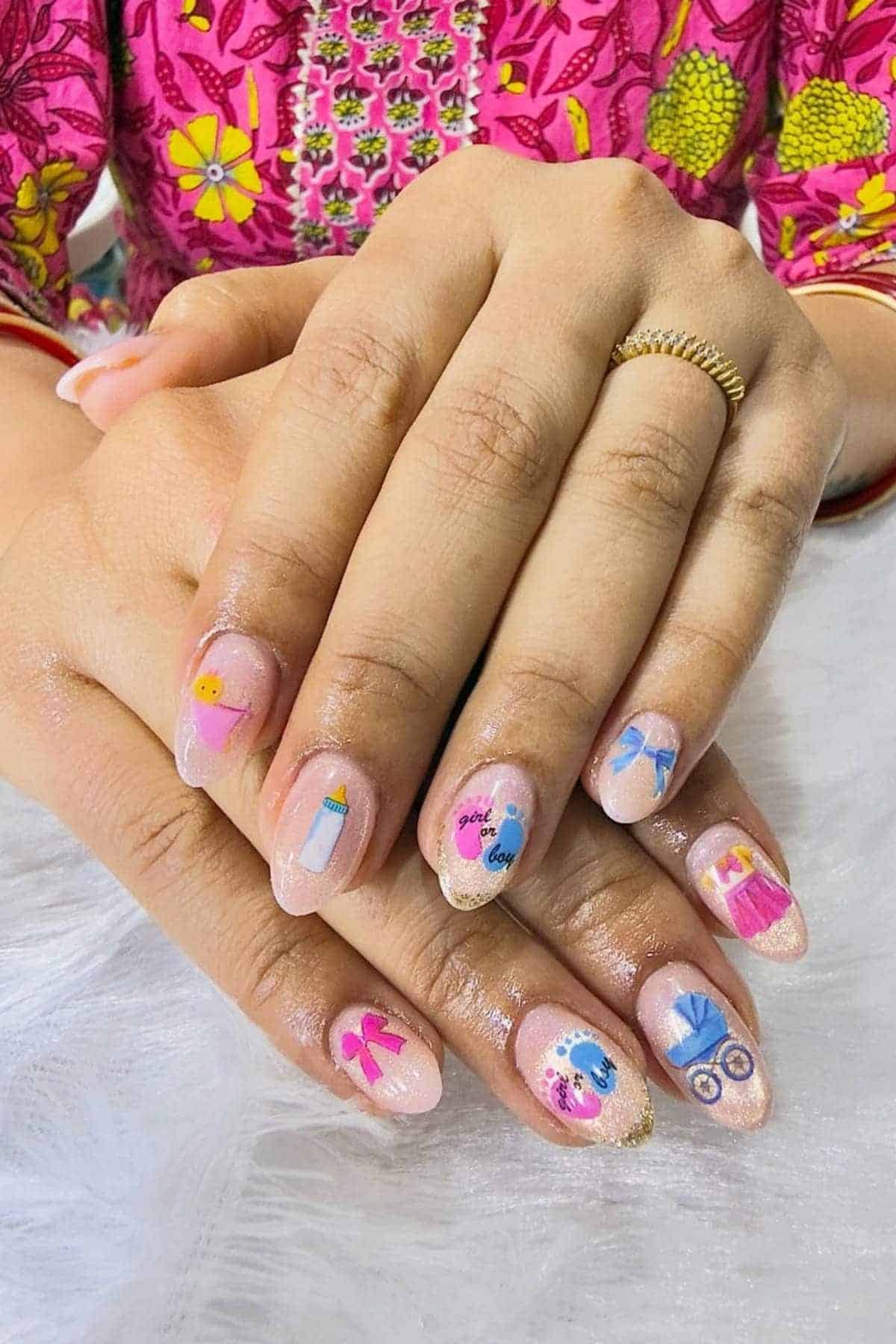 A person with neatly manicured nails featuring colorful baby-themed nail art, including bottles, bows, and baby faces, rests their hands on a white surface.
