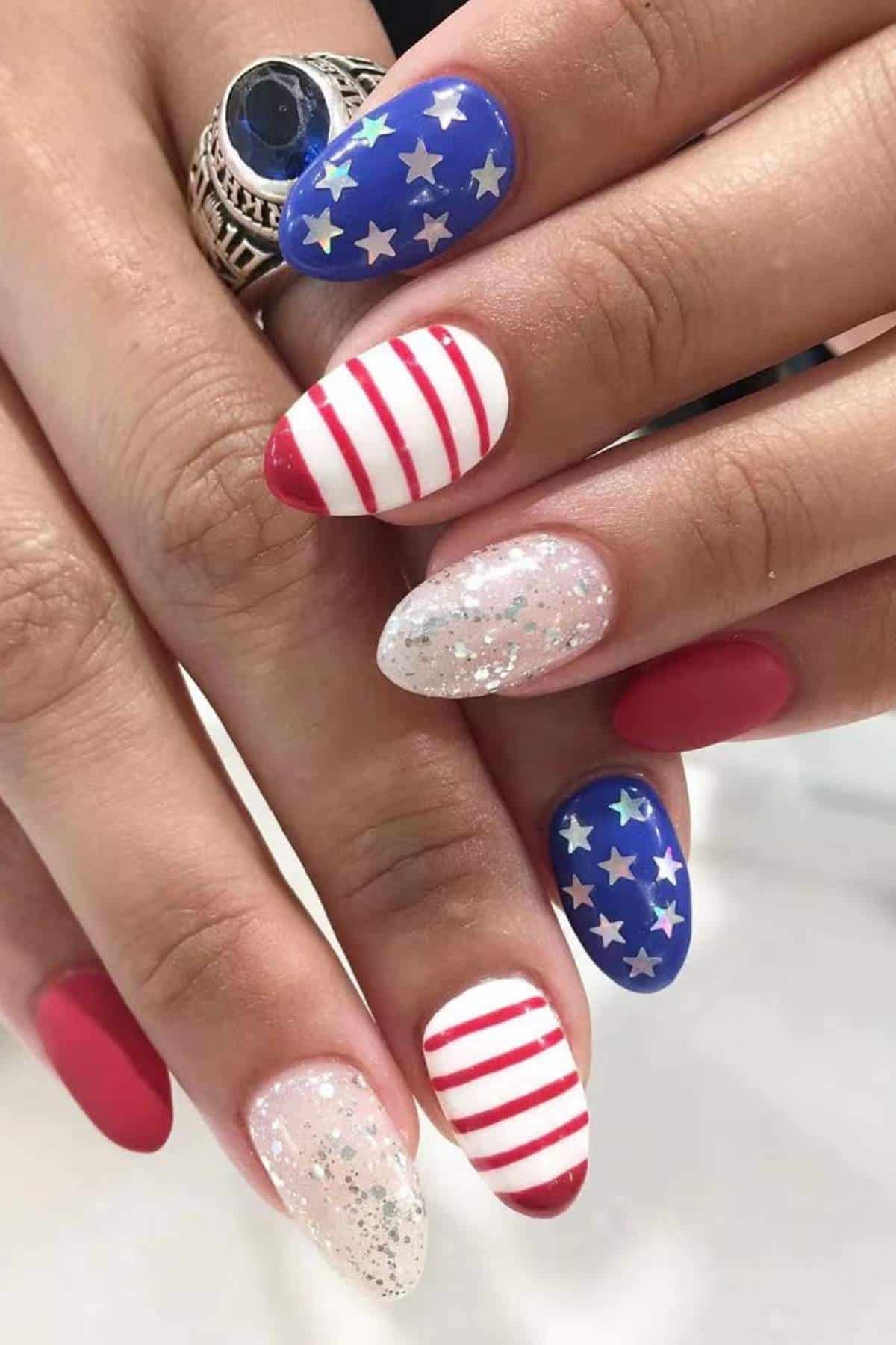 Close-up of hands with manicured nails featuring American flag designs, including stars, stripes, solid red, and glittery white patterns.