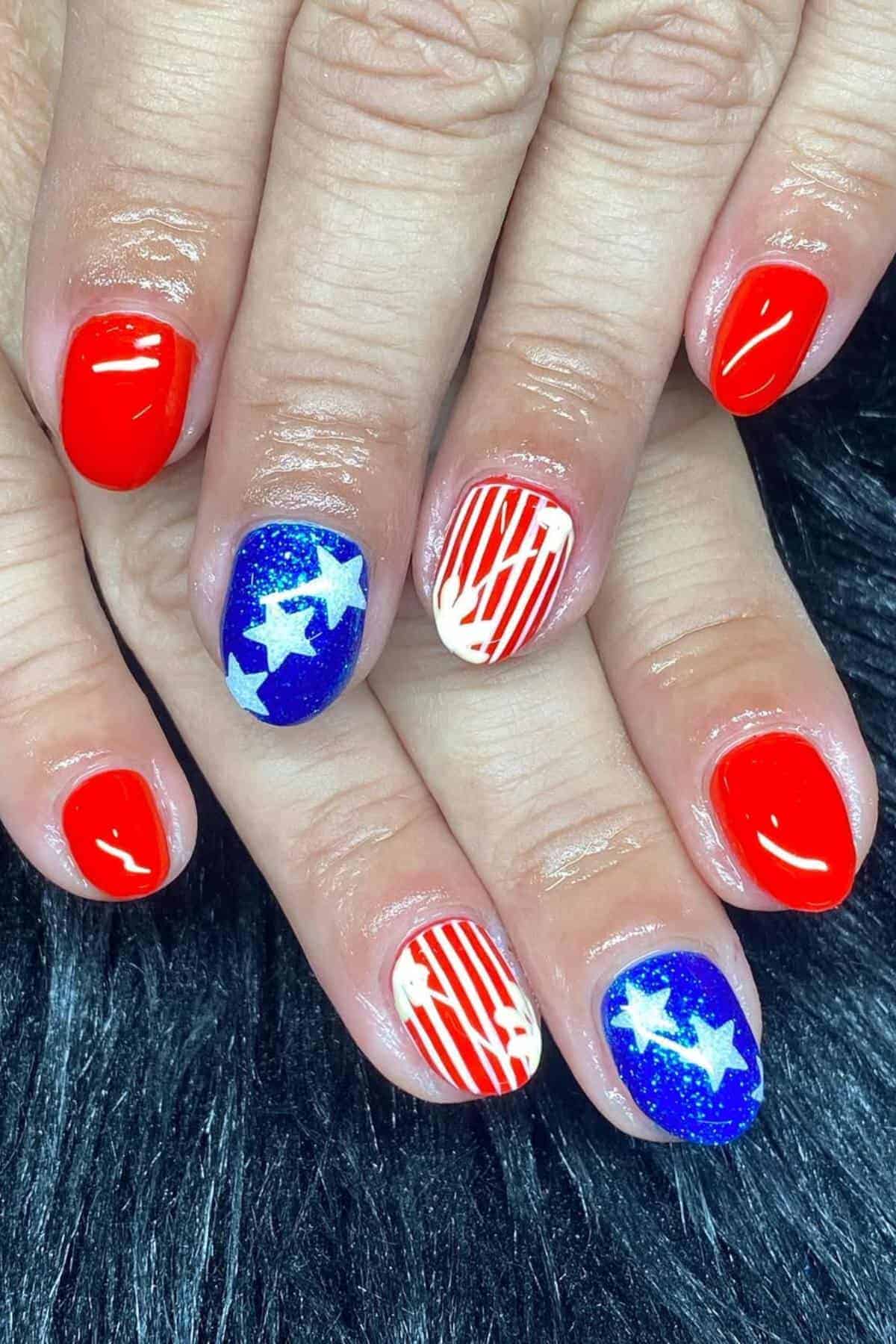 Hands with manicured nails featuring a red, white, and blue patriotic design; some nails have stars or stripes, while others are painted solid red.