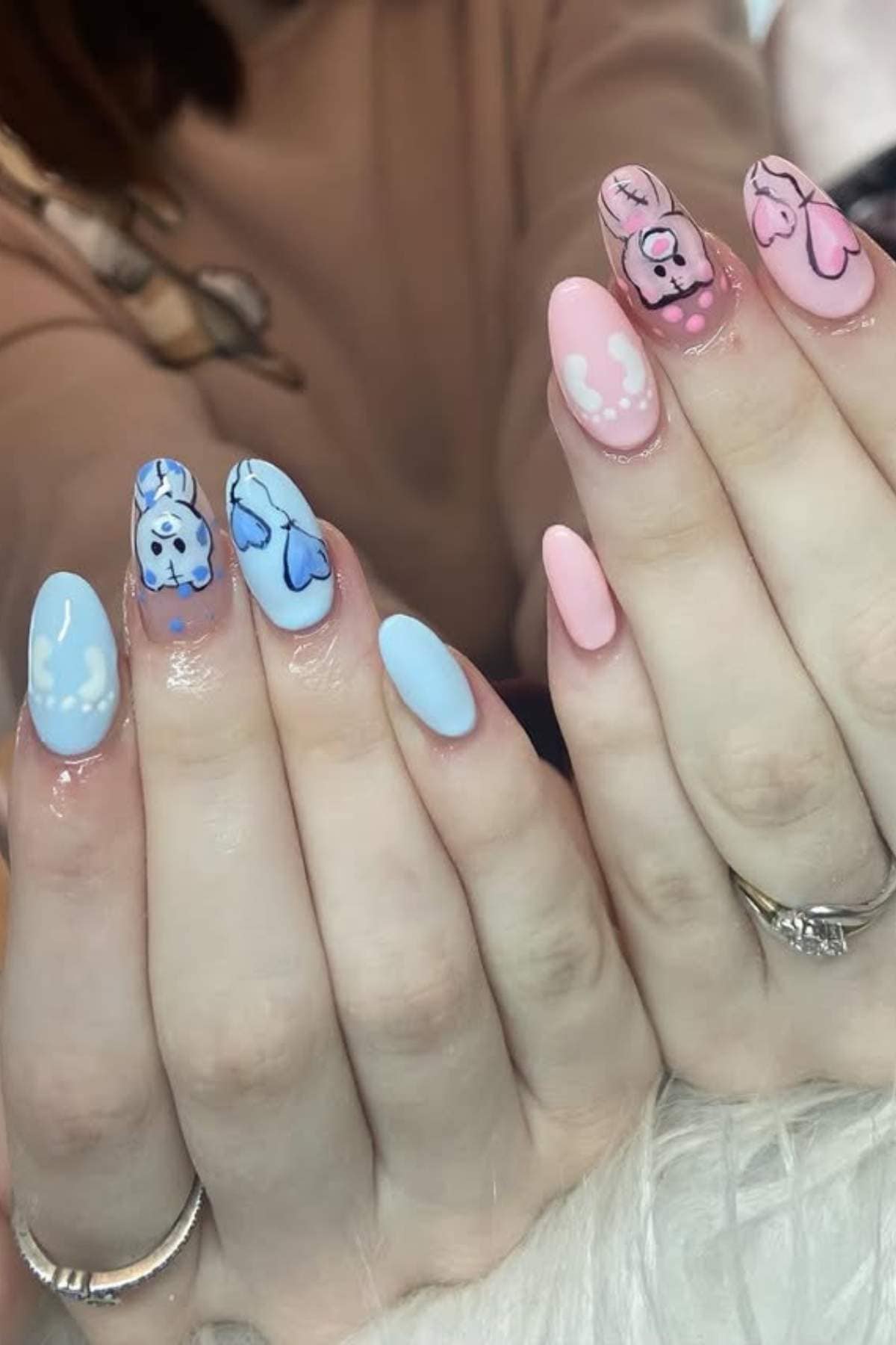 Hands with long manicured nails; left hand features blue polish with cartoon designs, right hand has pink polish with cartoon characters and white accents.