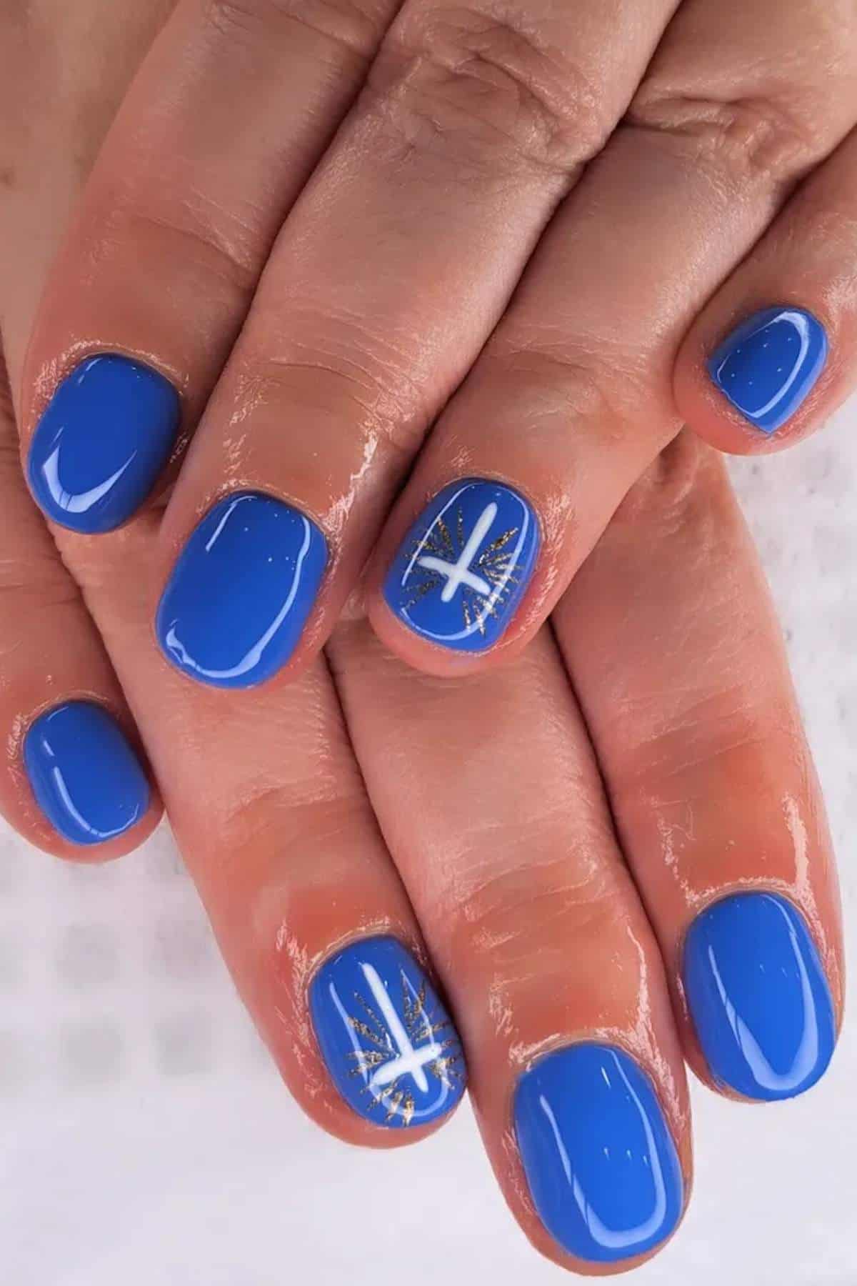 Hands with short, neatly manicured nails painted bright blue; two nails feature white star designs with gold accents.