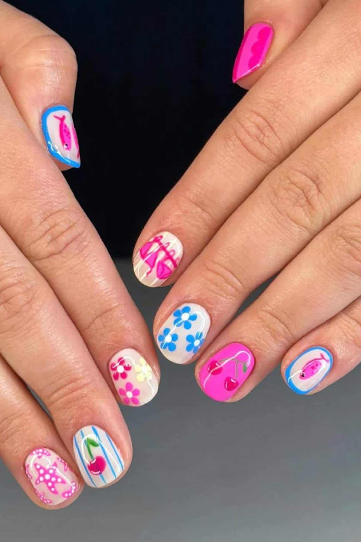 Hands with colorful nail art featuring cherries, flowers, stripes, and abstract designs on each fingernail.