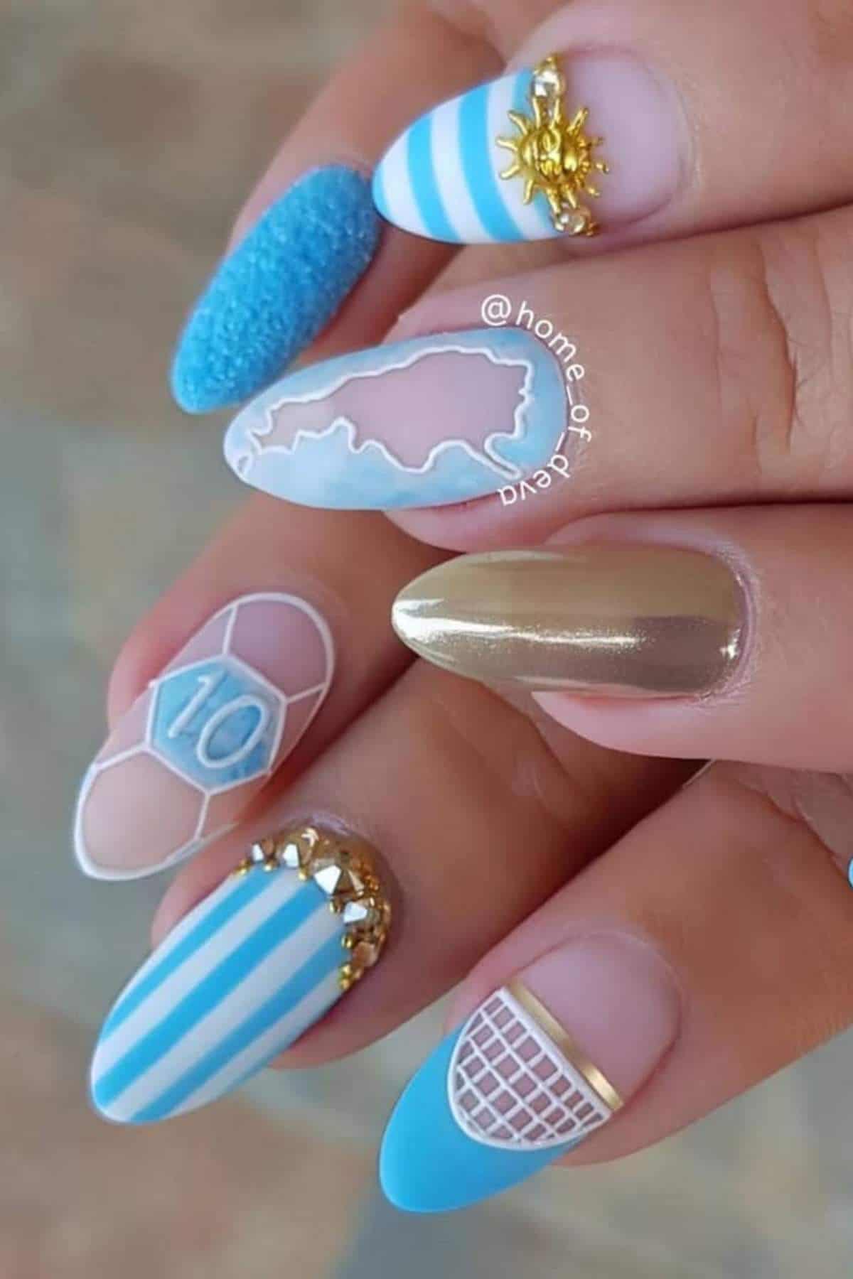 A hand with long, decorated nails featuring blue and white stripes, gold accents, a map outline, the number 10, net pattern, textured polish, and a sun design.