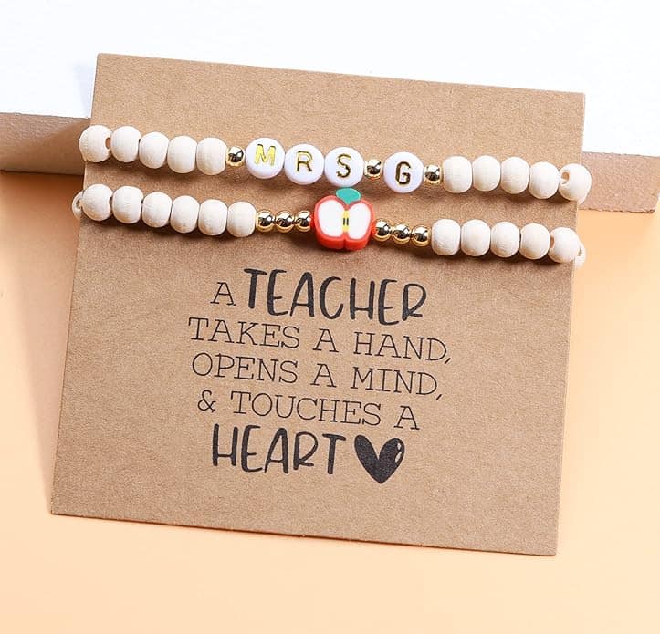 Two beaded bracelets with "MRS G" and an apple charm are displayed on a card that reads, "A teacher takes a hand, opens a mind, & touches a heart.