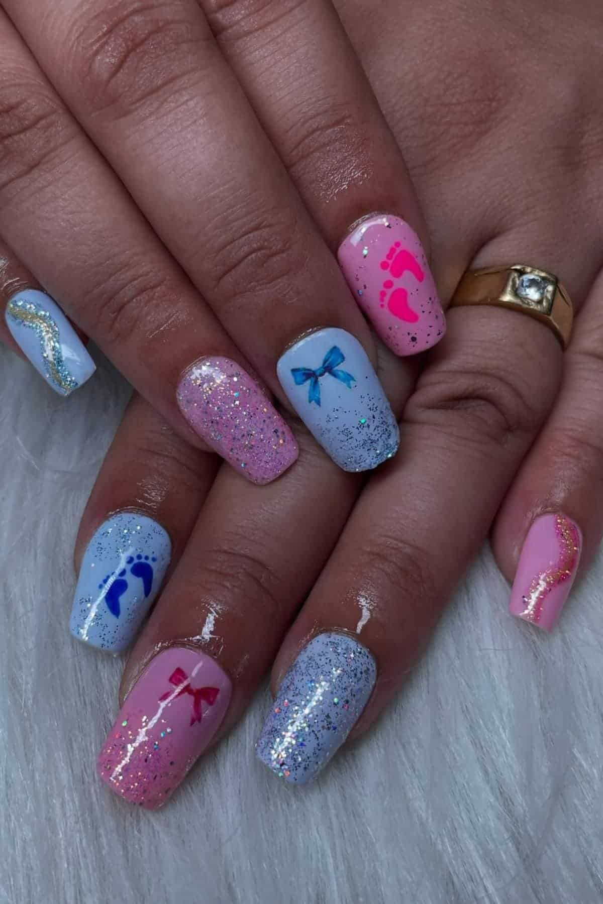 Close-up of hands with manicured nails in pastel pink and blue shades, decorated with glitter, bows, and small footprint designs.