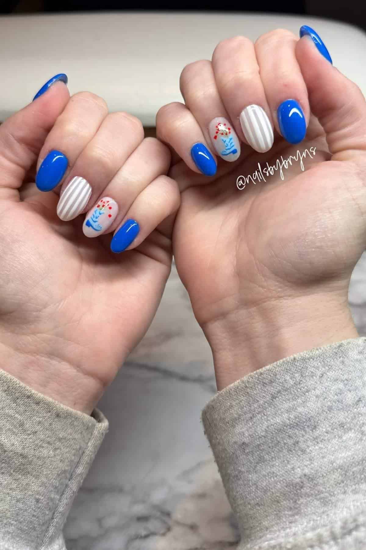 Hands with blue and white manicured nails; some nails feature red and blue flower designs and white stripes.