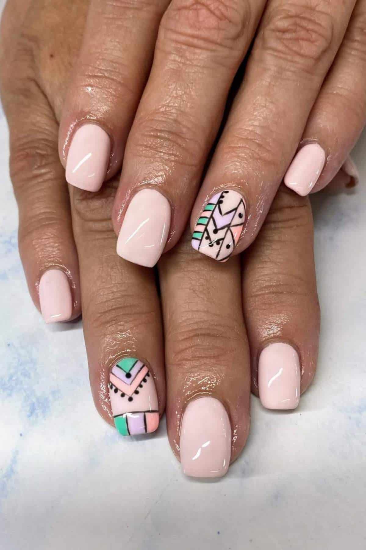 Hands with short, light pink manicured nails; two accent nails feature geometric patterns in black, green, and pink.