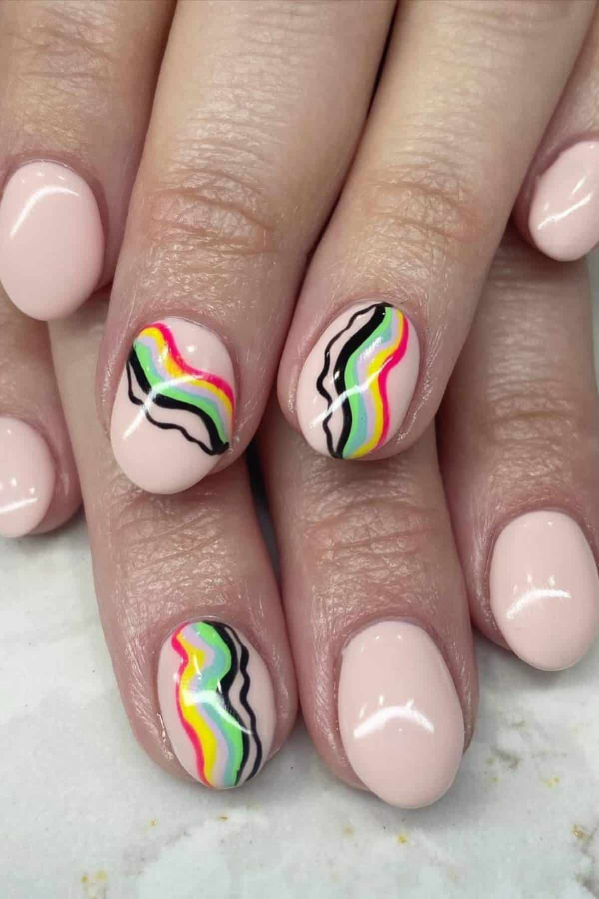 Close-up of hands with light pink nail polish; two accent nails feature wavy lines in black, yellow, green, and pink.