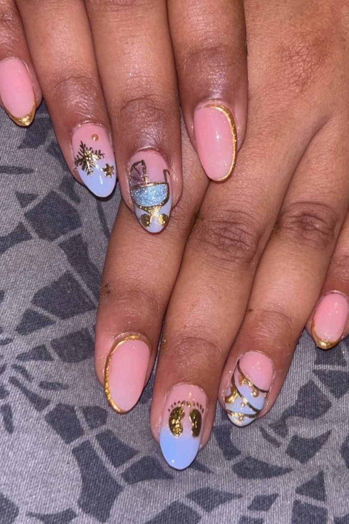 Hands with short, almond-shaped nails featuring pink and light blue polish, gold accents, and various decorative nail art designs.