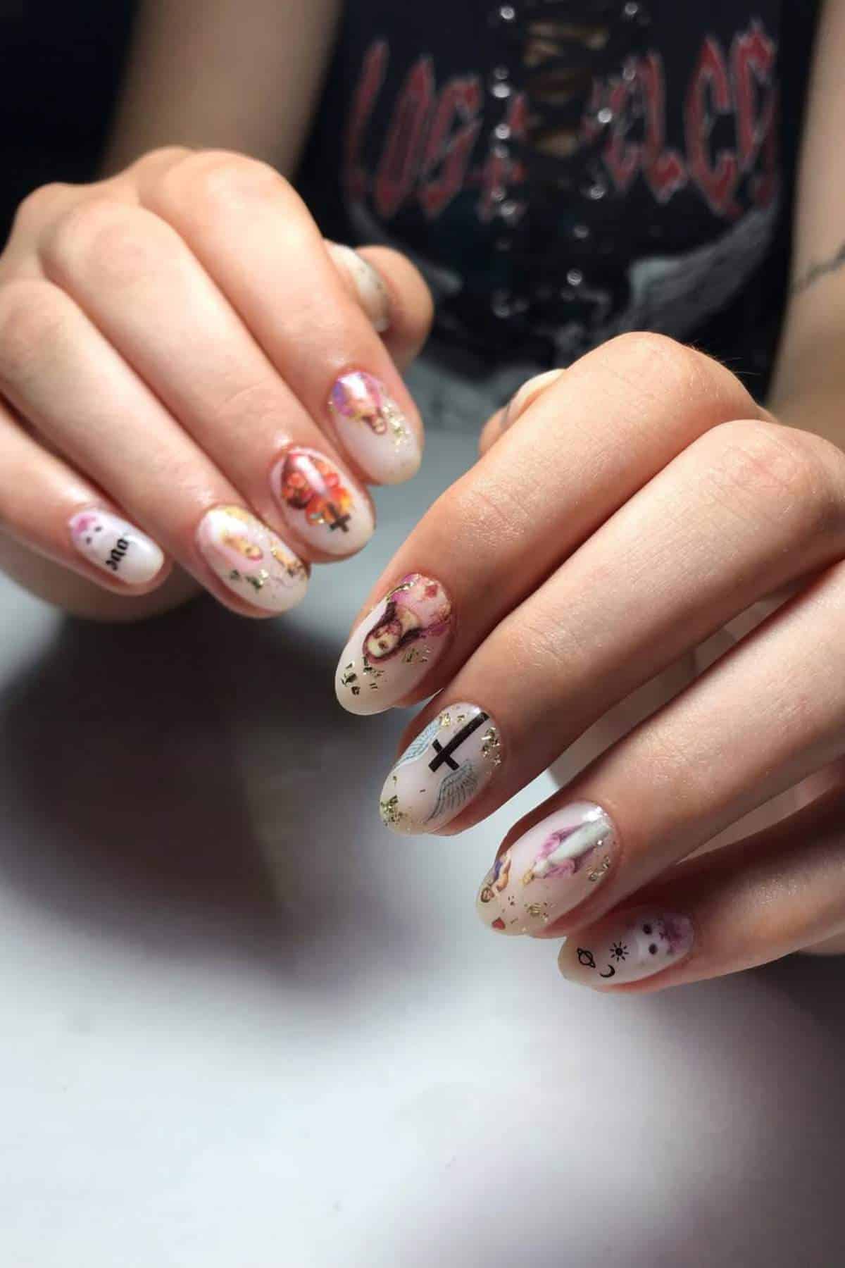 Close-up of hands with long, almond-shaped nails featuring detailed, colorful art designs, including faces, crosses, flowers, and gold accents.