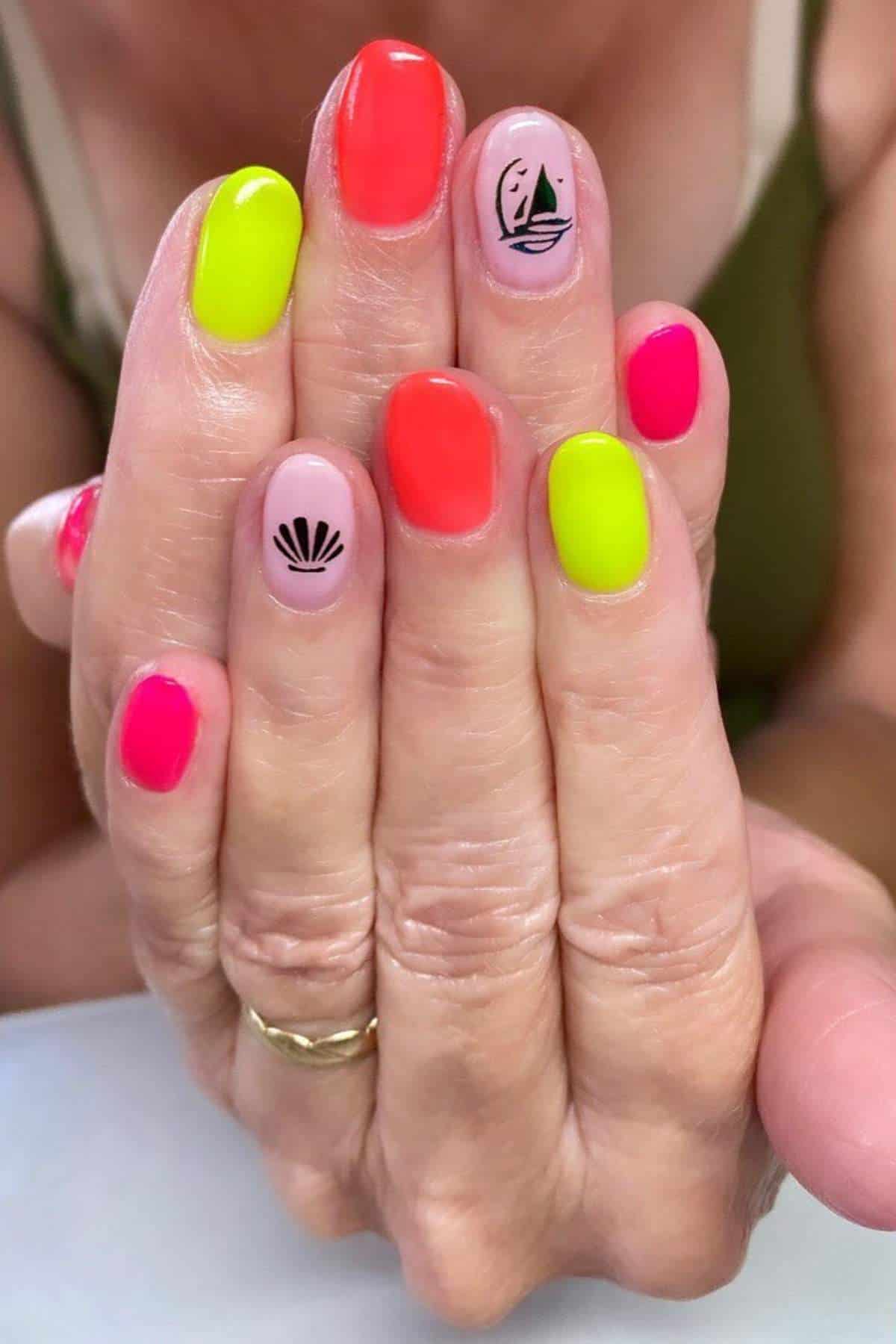 Close-up of hands with brightly colored manicure in neon pink, yellow, and orange; two nails feature black designs of a shell and a sailboat.