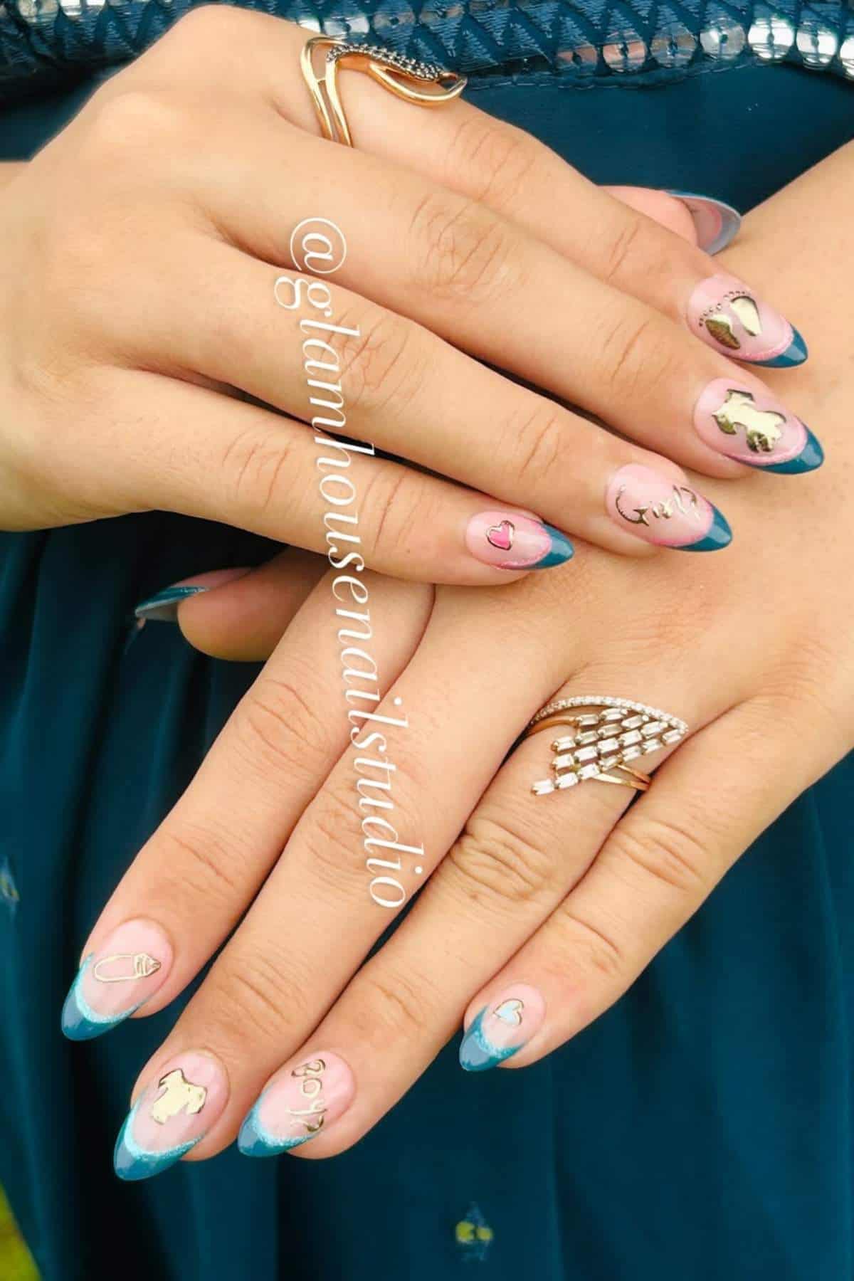 Close-up of hands with blue French tip nails, gold animal and heart decals, and rings on fingers, with "@glamhouse_nailstudio" text on the image.