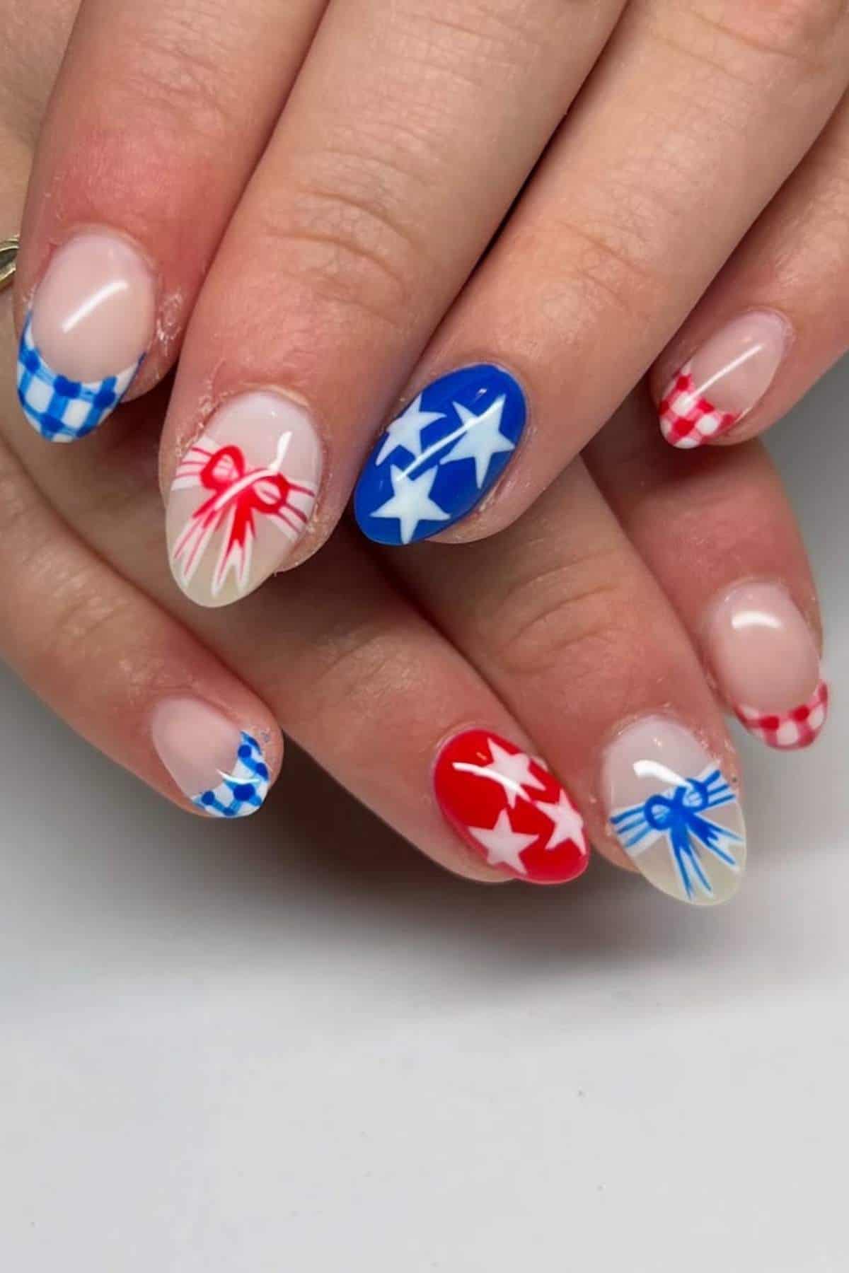 Hands with manicured nails featuring red, blue, and white designs, including stars, bows, and gingham patterns on a neutral background.