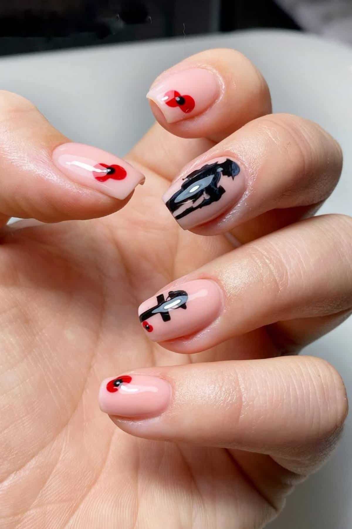 A hand with nude-colored nails featuring black abstract designs and small red dots as accents on each nail.
