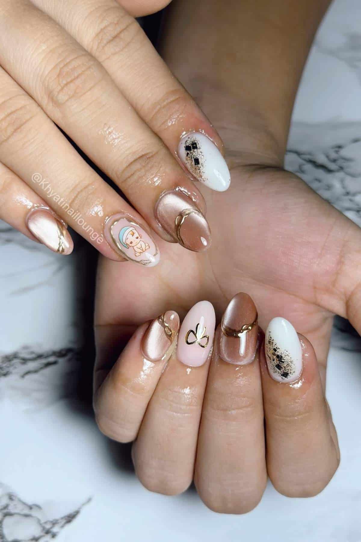 A close-up of hands with almond-shaped nails featuring a mix of nude, white, and brown polish, gold accents, abstract designs, and a cartoon character on one nail.