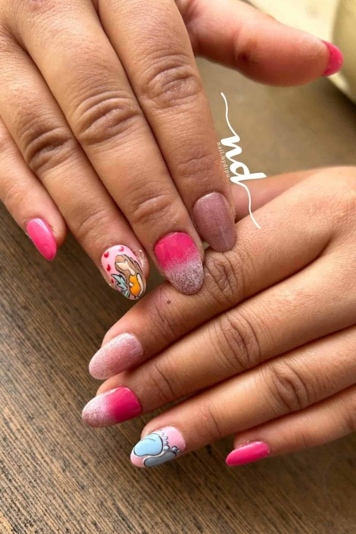 Hands with manicured nails featuring pink and ombre designs, with two nails on each hand decorated with cartoon-style artwork.