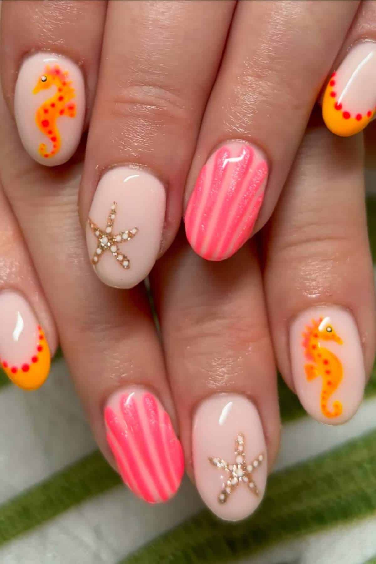 Close-up of hands with nail art featuring yellow and pink seahorses, beige starfish, and pink striped designs on a light nude base.
