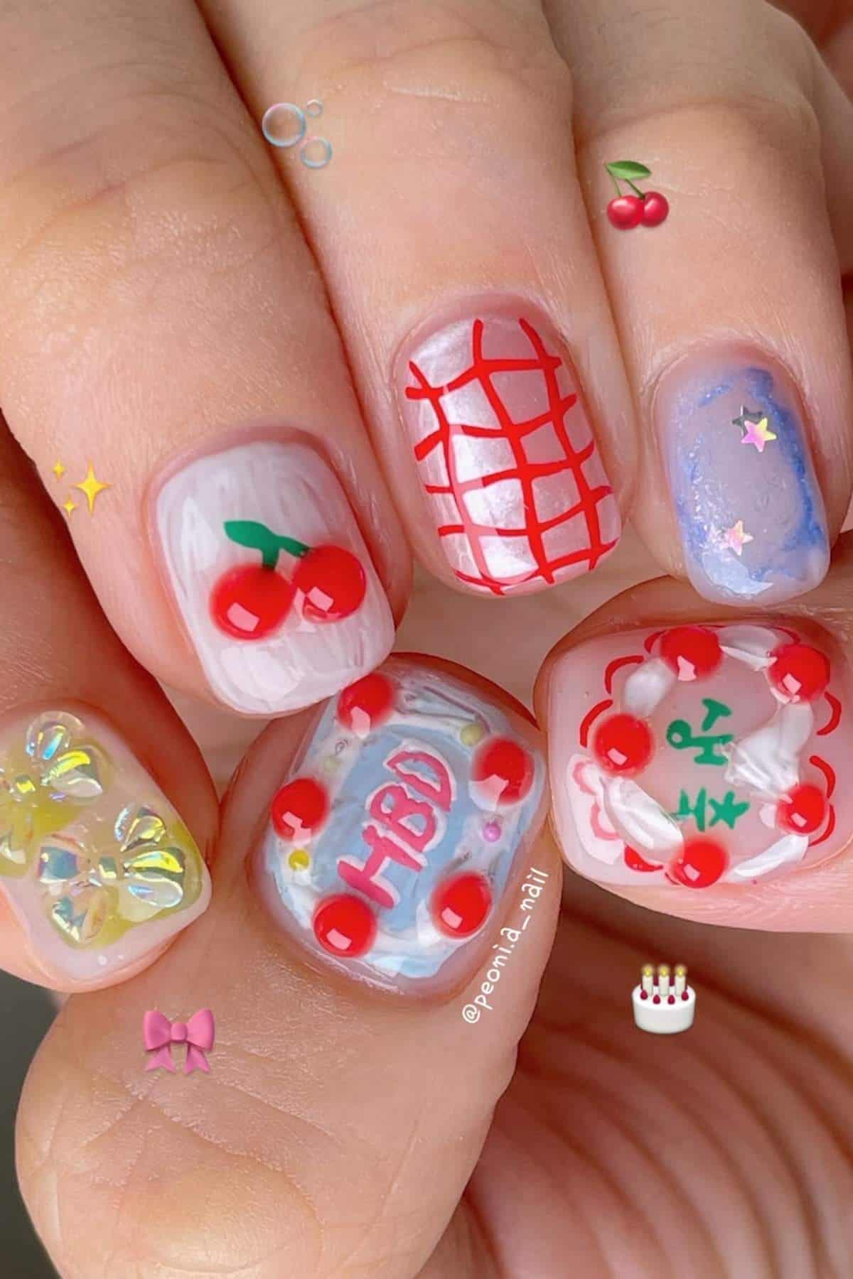 Close-up of a hand with colorful nail art featuring cherries, a red grid pattern, swirls, 3D flowers, and decorative details on each fingernail.
