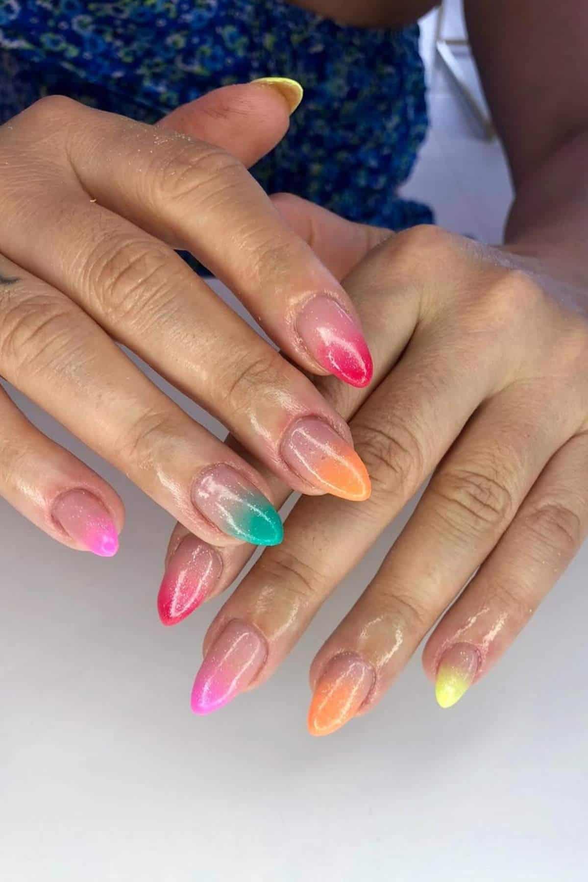 A person displays manicured hands with long almond-shaped nails, each painted a different bright color with a gradient effect.