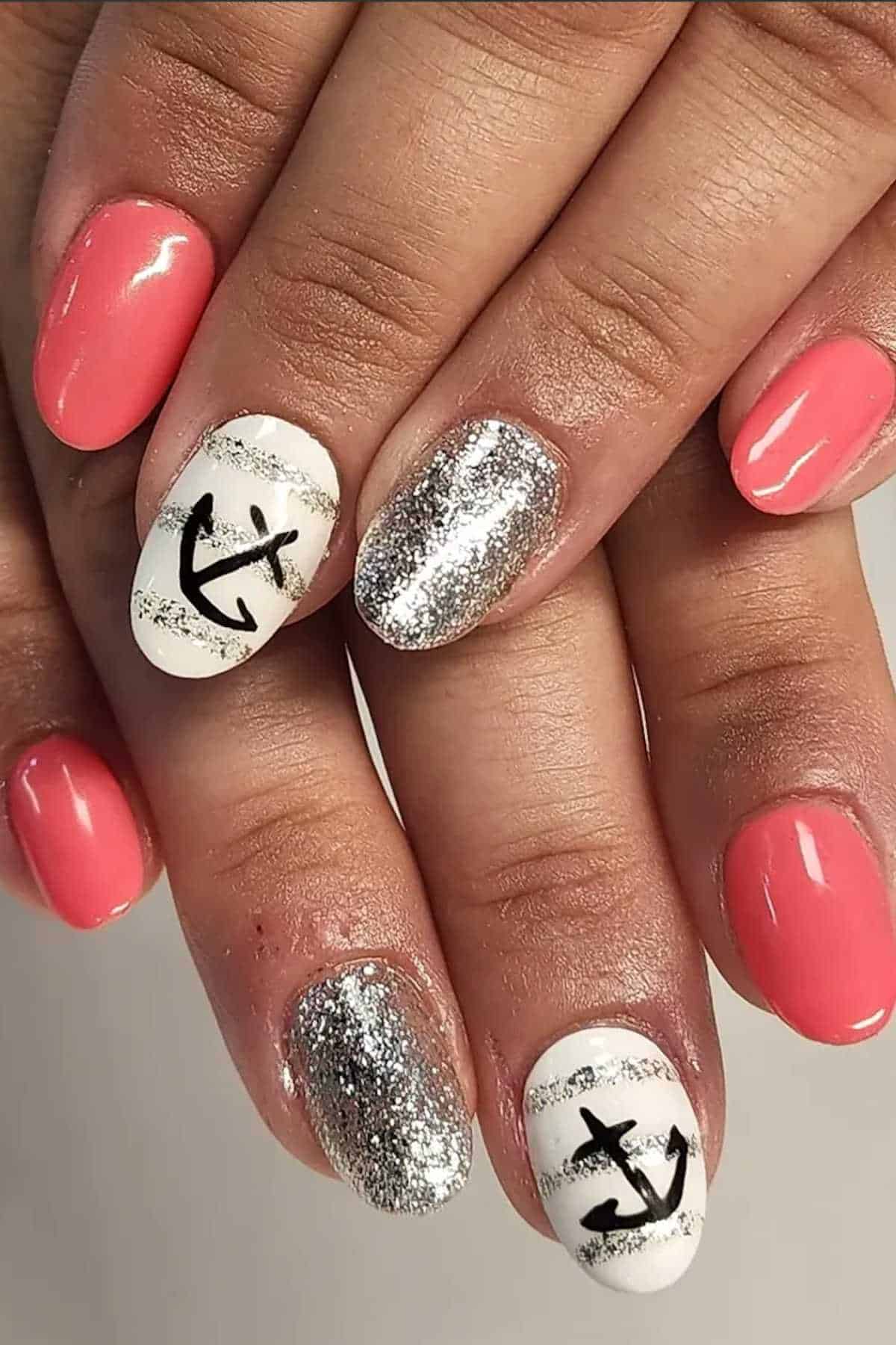 Hands with manicured nails featuring pink polish, silver glitter, and white accent nails with horizontal stripes and black anchor designs.