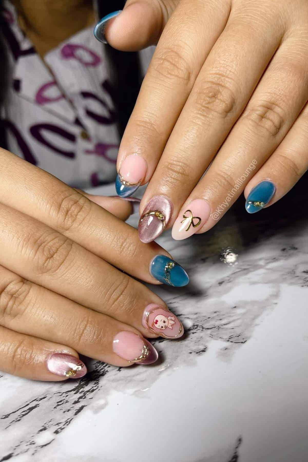 A person with multicolored manicured nails featuring blue, pink, nude, gold accents, a bow charm, and a cartoon bear design, resting on a marble surface.
