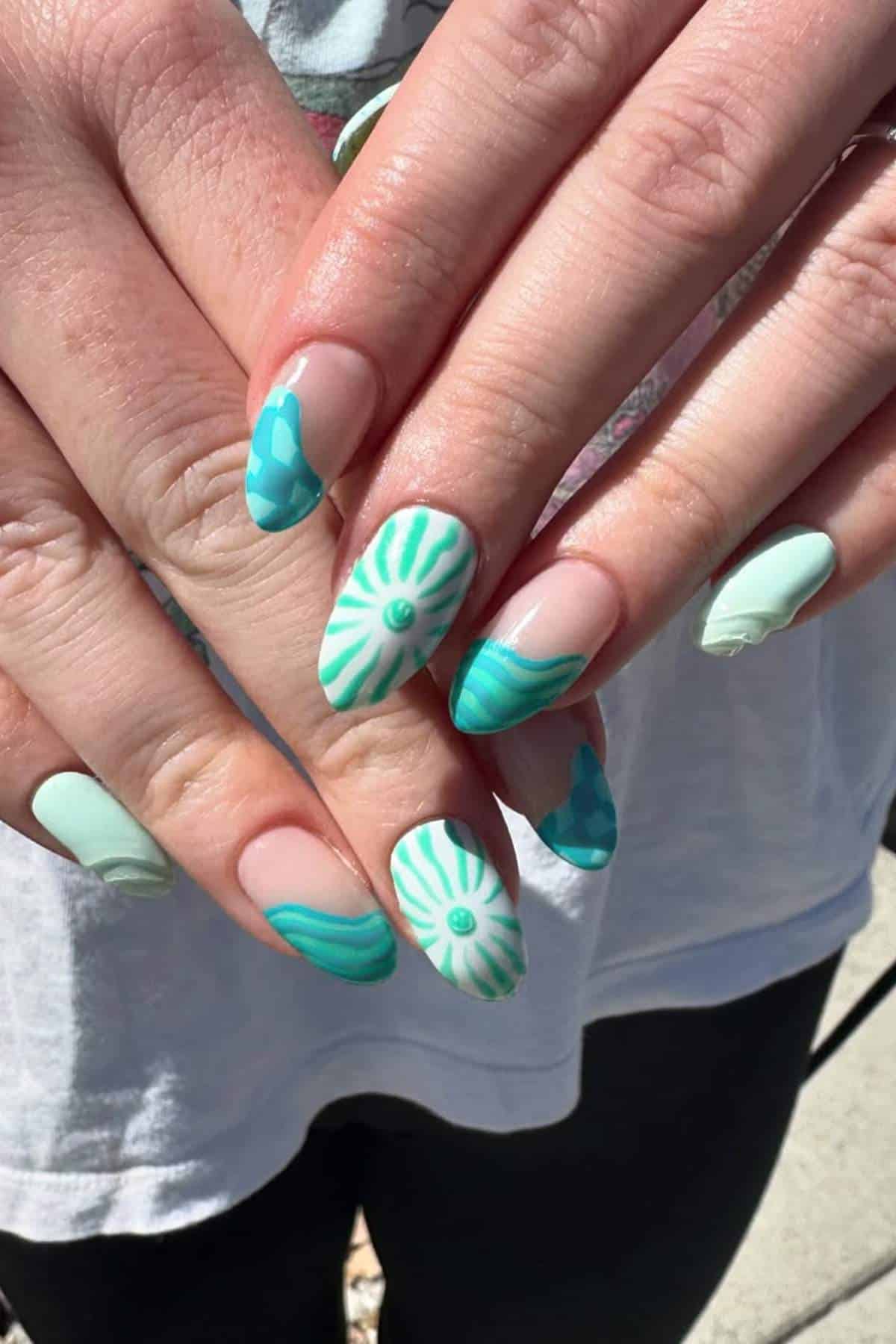 Hands with almond-shaped nails painted in mint green and turquoise designs, including stripes, flowers, and abstract patterns.