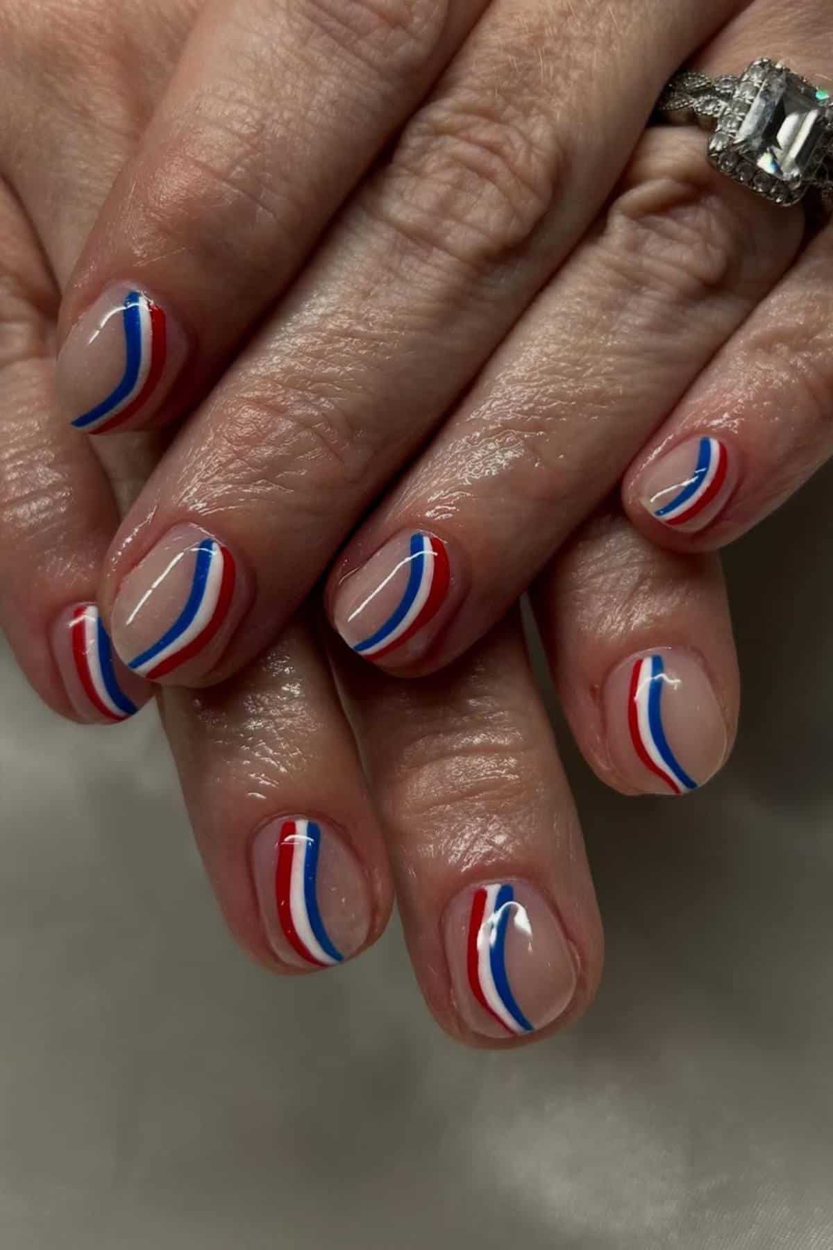 Close-up of hands with short nails featuring a minimalist design of curved red, white, and blue lines on a nude base.