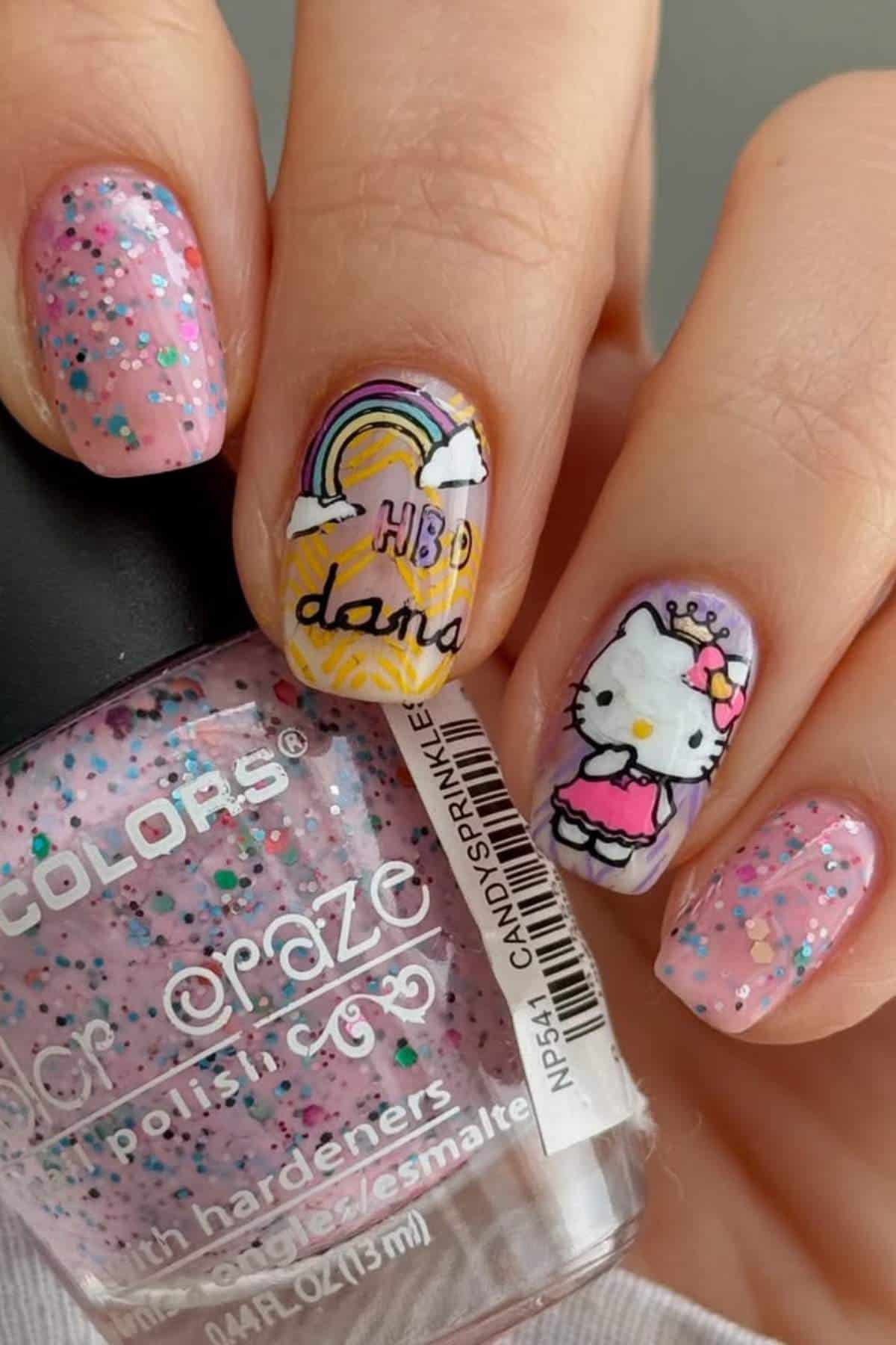 A hand with pink glittery nail polish; two nails feature detailed art of a rainbow with "HBD Dana Vasu" and a Hello Kitty character in a pink dress and crown.