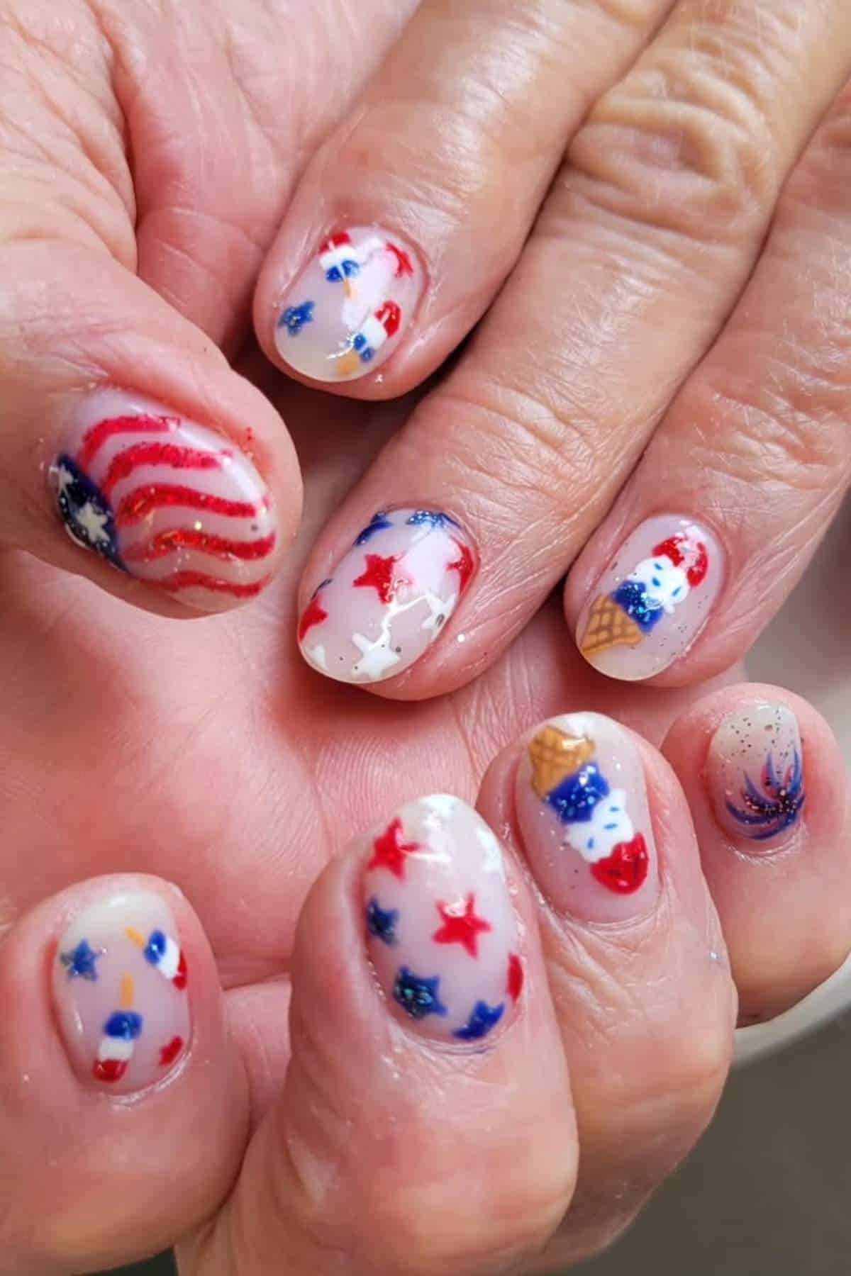 Fingernails with patriotic nail art designs featuring American flags, stars, fireworks, and red, white, and blue colors.