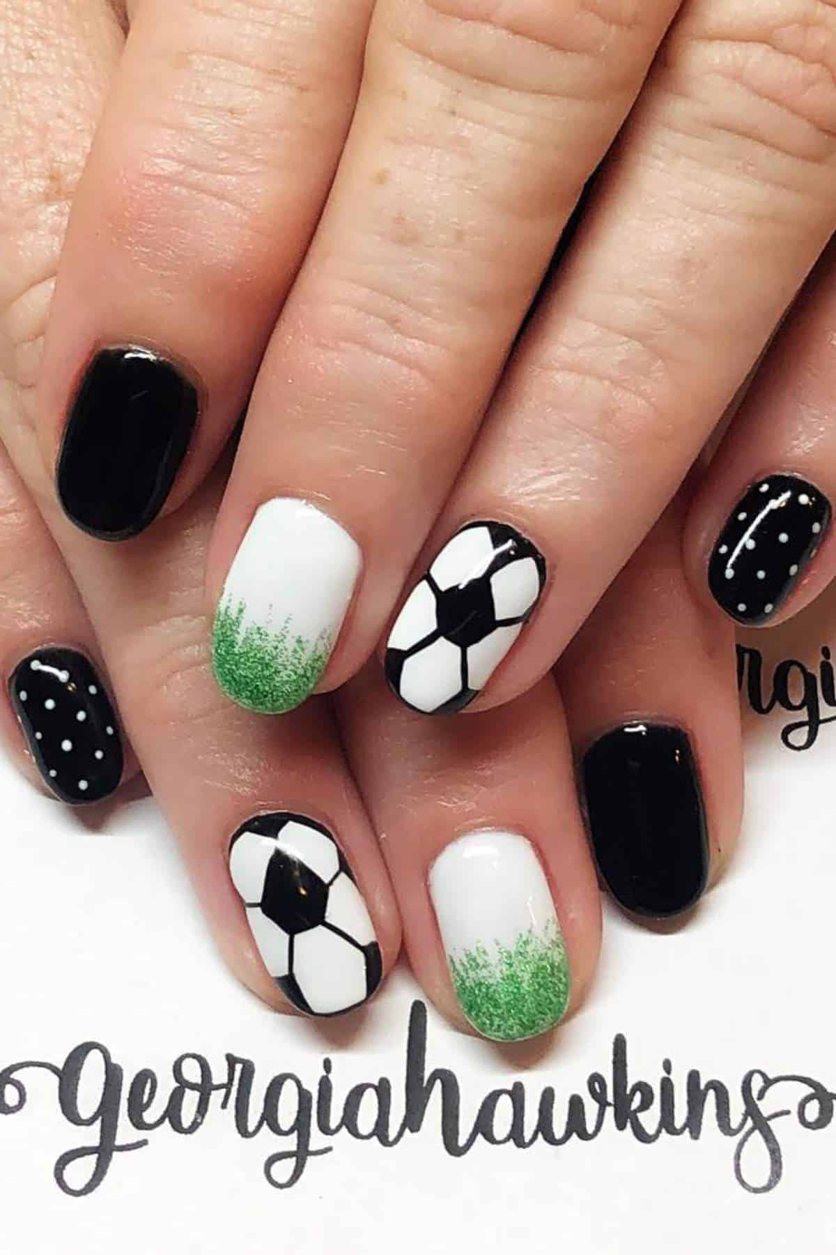 Hands with short nails painted in a soccer theme, featuring black, white, green, and soccer ball designs on alternating nails.