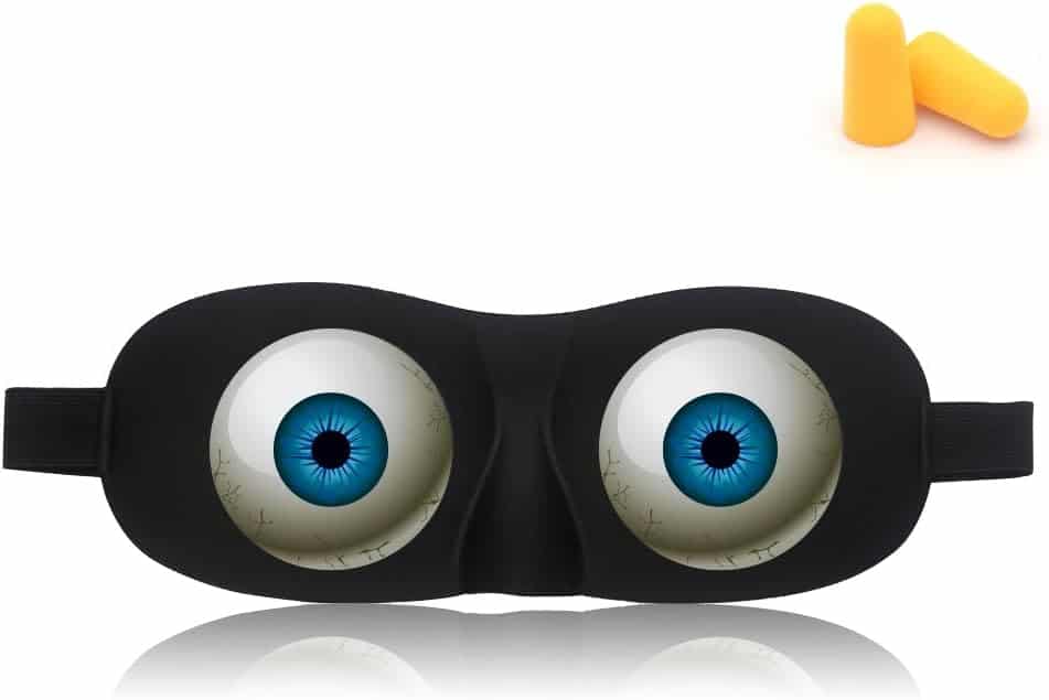 Black sleep mask with realistic blue eye designs on the front, accompanied by a pair of orange foam earplugs in the upper right corner.