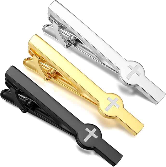 Three metal tie clips in silver, gold, and black, each with an engraved cross design, are displayed side by side on a white background.