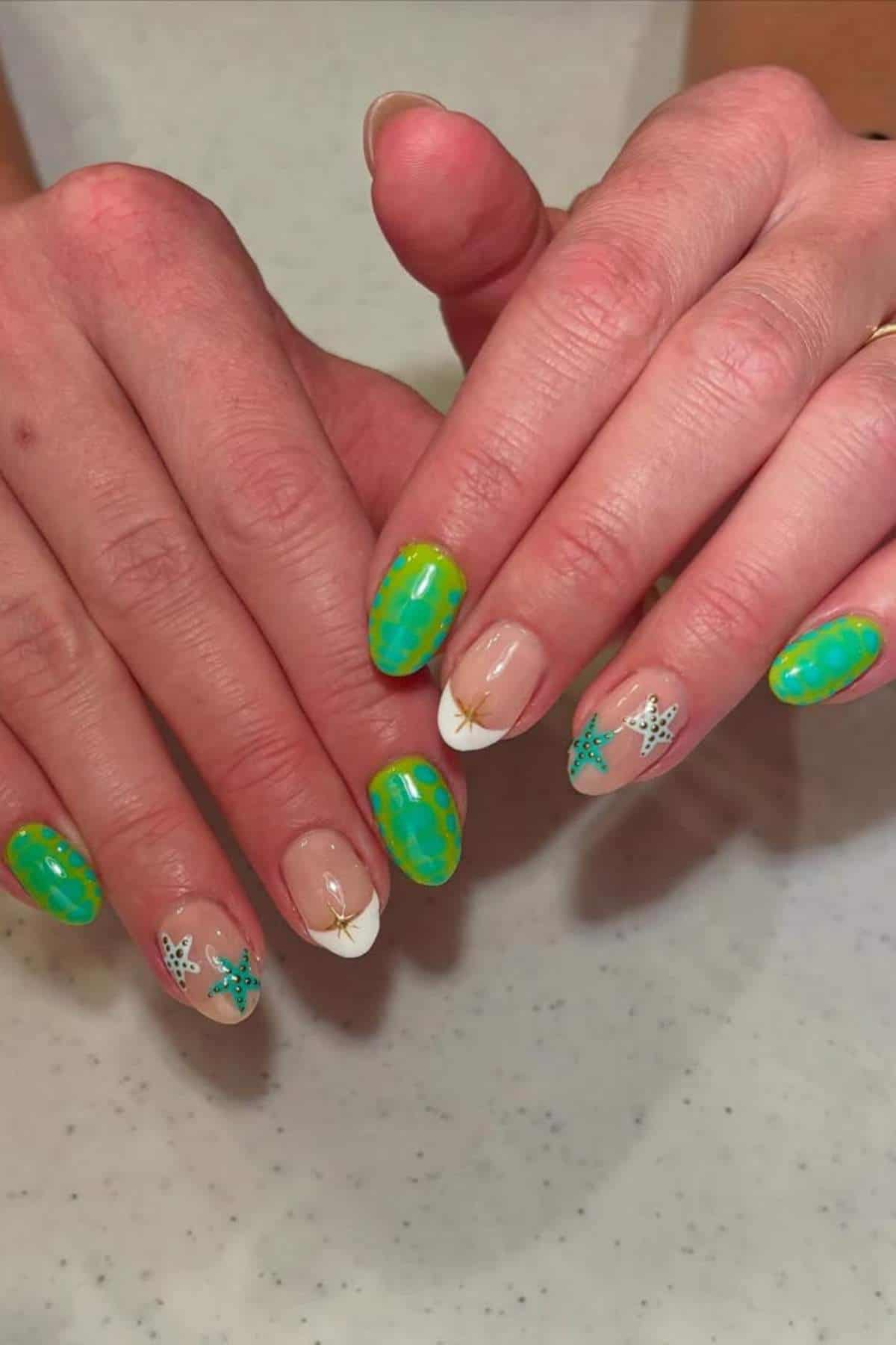 Hands with manicured nails; some nails have green and yellow patterns while others feature white tips and small blue starfish designs.
