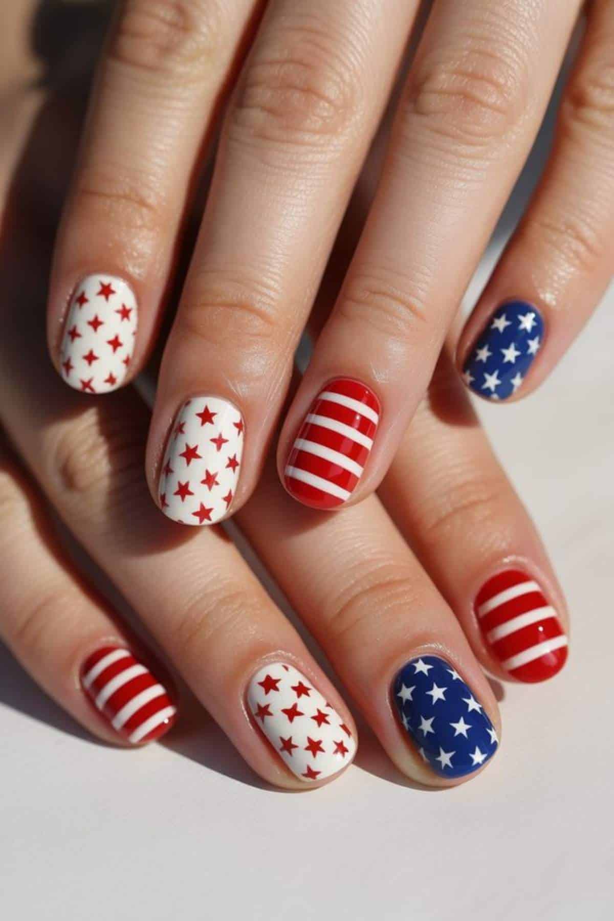 Hands with fingernails painted in red, white, and blue designs featuring stars and stripes resembling the American flag.