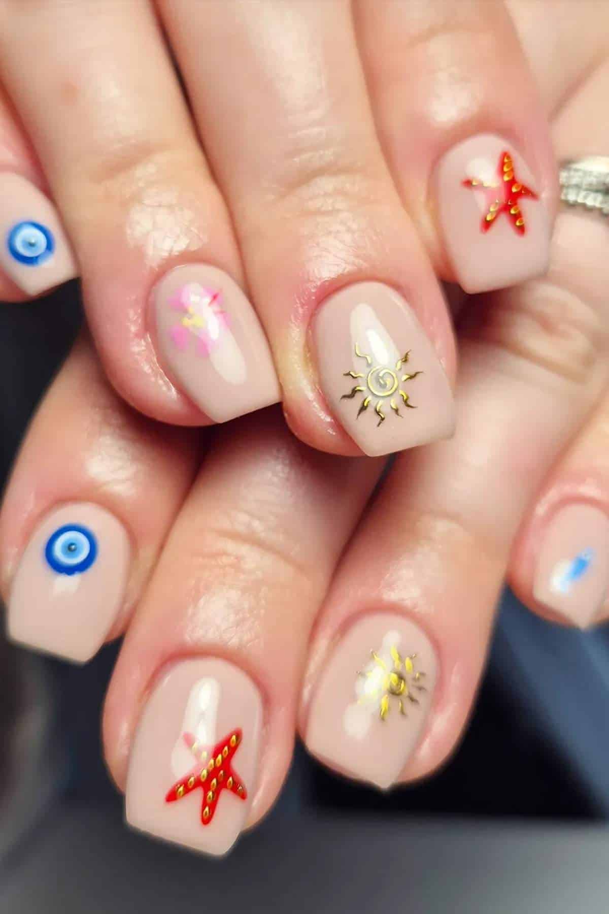 Close-up of hands with nude-colored nail polish, each nail decorated with different colorful designs including stars, flowers, eyes, and sun patterns.