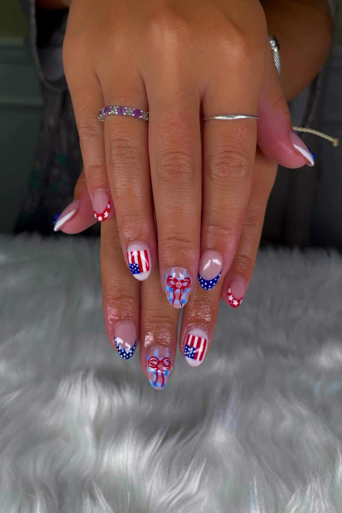Hands with manicured nails featuring red, white, and blue designs, including stars, stripes, and bows reminiscent of the American flag.