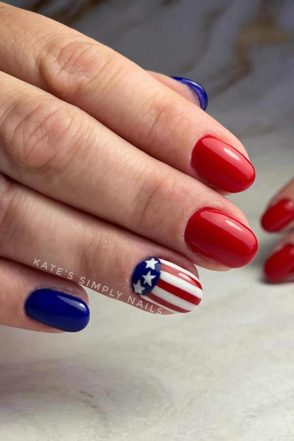 A hand with manicured nails painted red, blue, and one with an American flag design featuring white stars and red and white stripes.