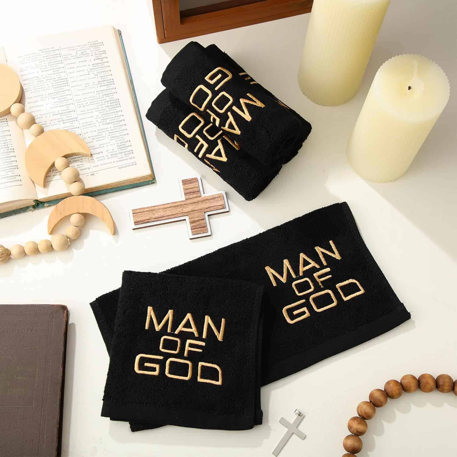 Black towels embroidered with "MAN OF GOD" are displayed on a table alongside candles, a Bible, a rosary, wooden crosses, and other religious items.